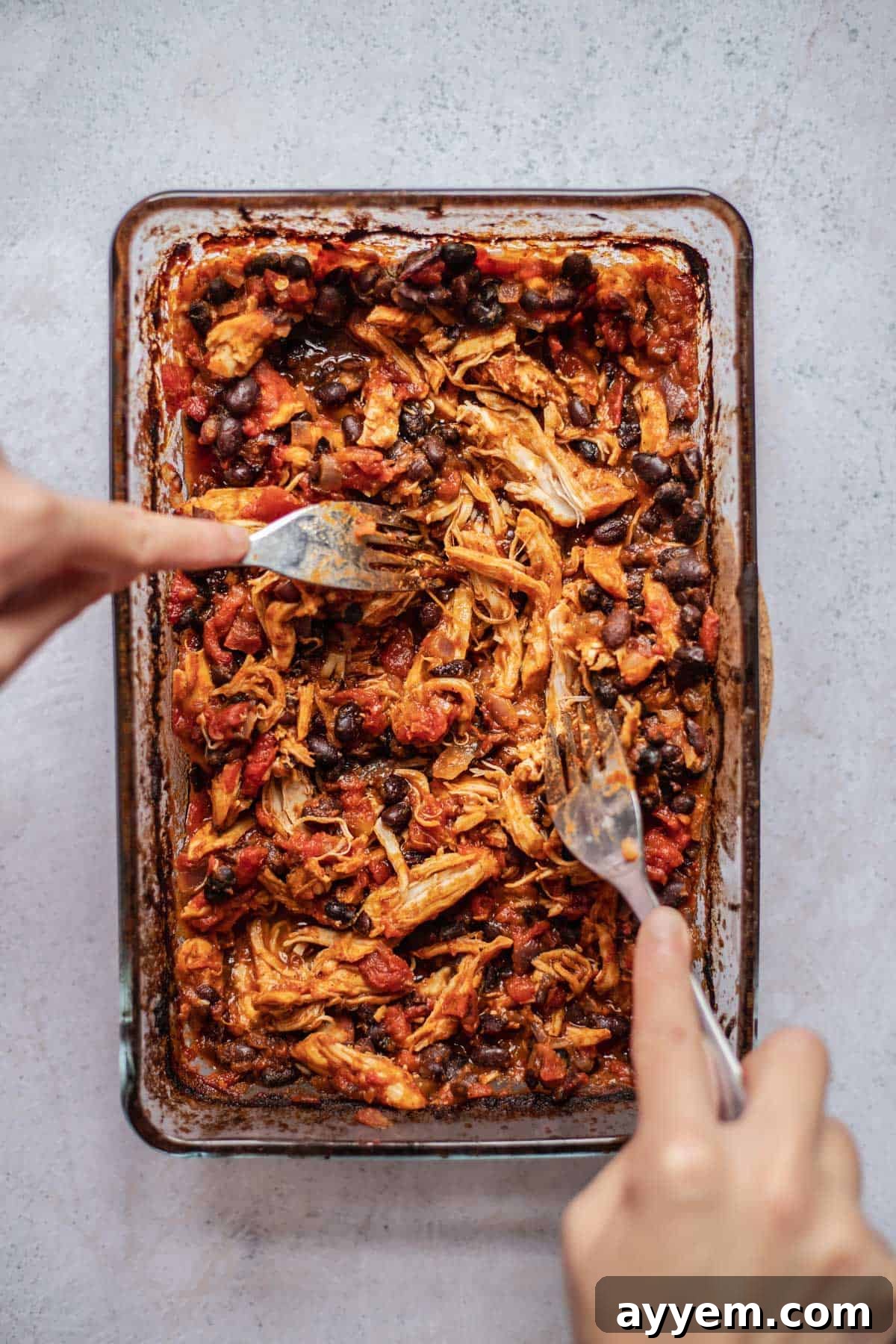 two hands using forks to shred chicken taco meat