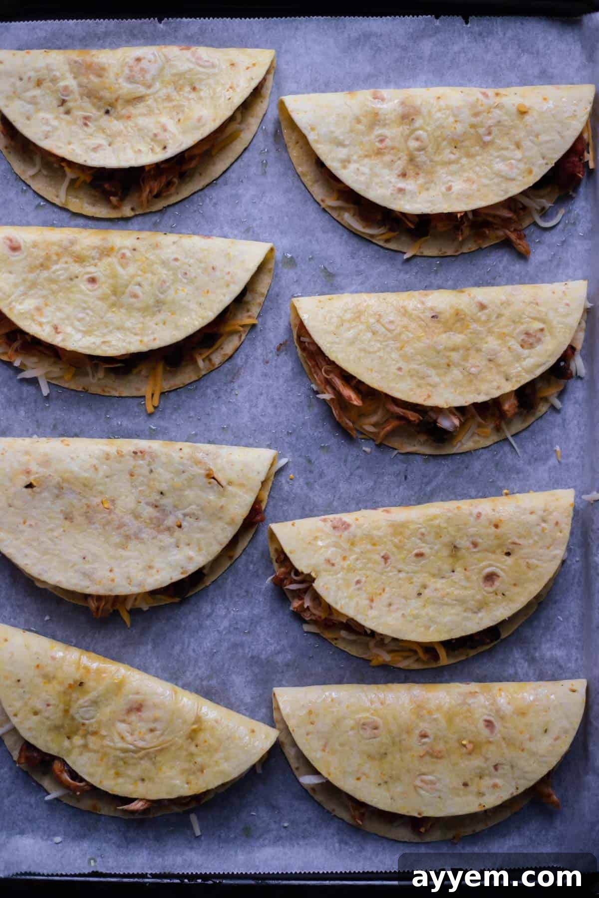 taco shells stuffed with shredded chicken on a parchment-lined baking sheet