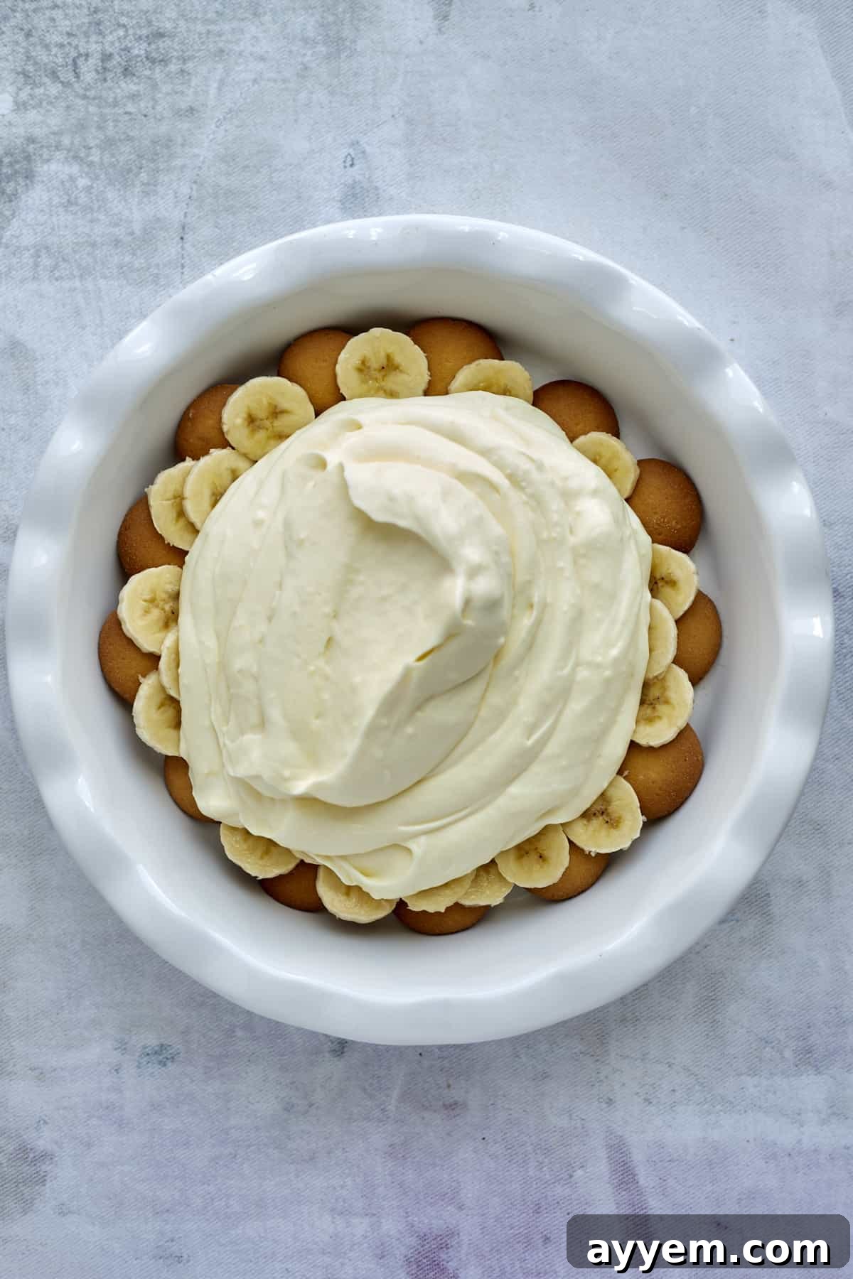 A generous pour of creamy vanilla pudding filling covering the banana and wafer layers in a baking dish.
