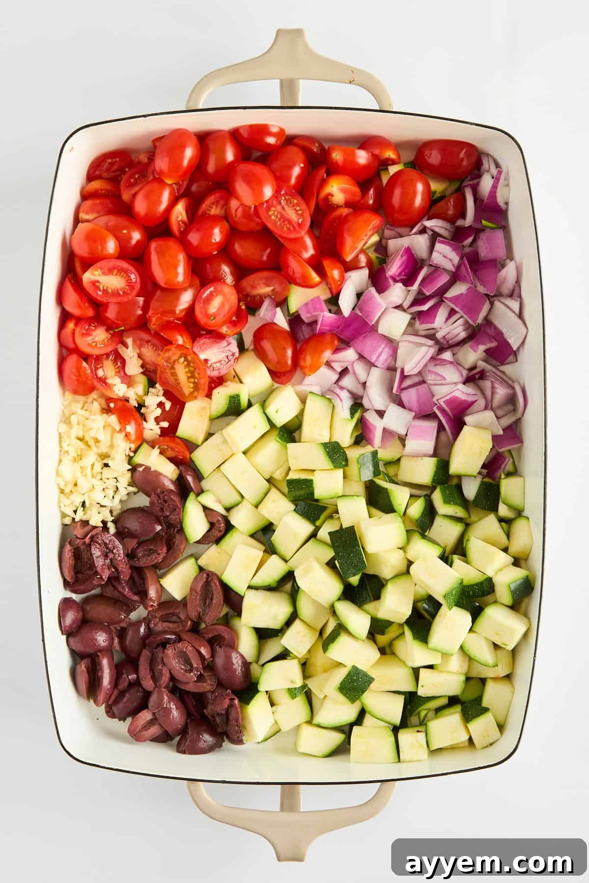 Cherry tomatoes, zucchini, and Kalamata olives arranged in a baking dish before cooking.