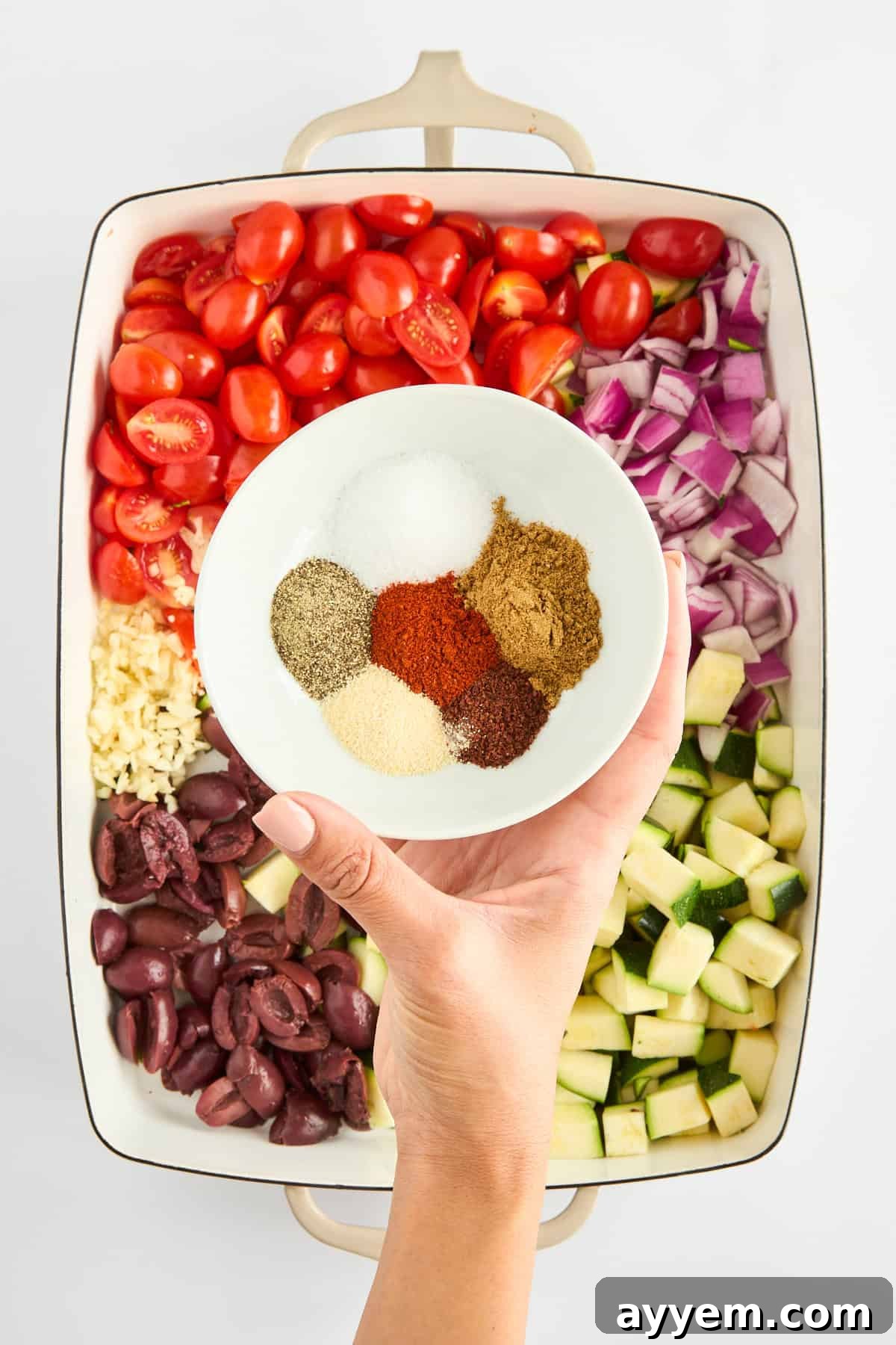 A mix of aromatic spices being sprinkled over the vegetables in a baking dish.