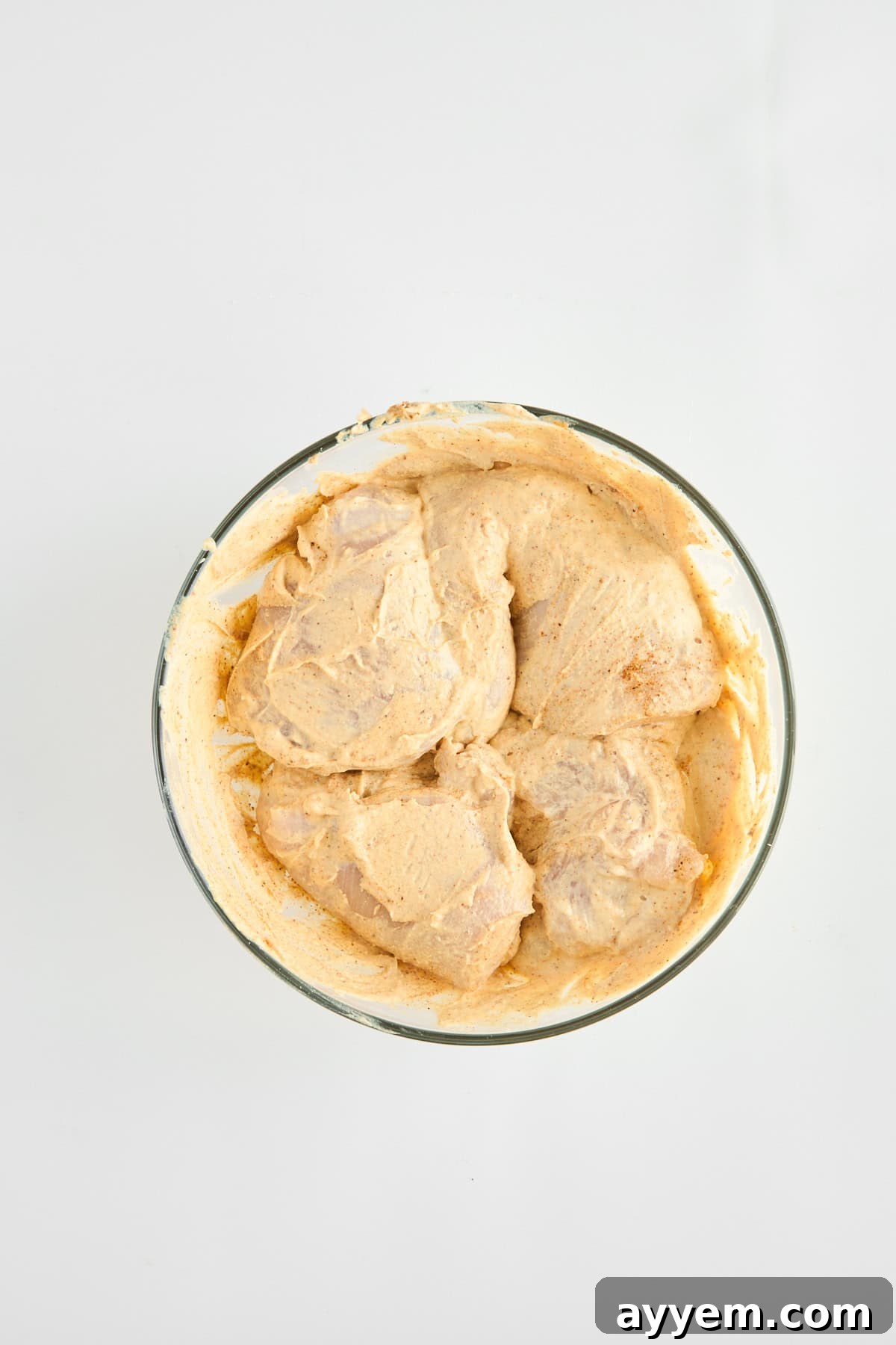 Pounded chicken breasts covered with hummus in a baking dish with vegetables.