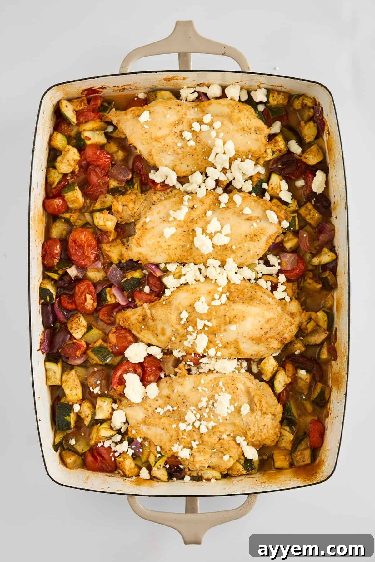 Hummus Baked Chicken in a baking dish, perfectly cooked with golden hummus and roasted vegetables topped with melted feta.