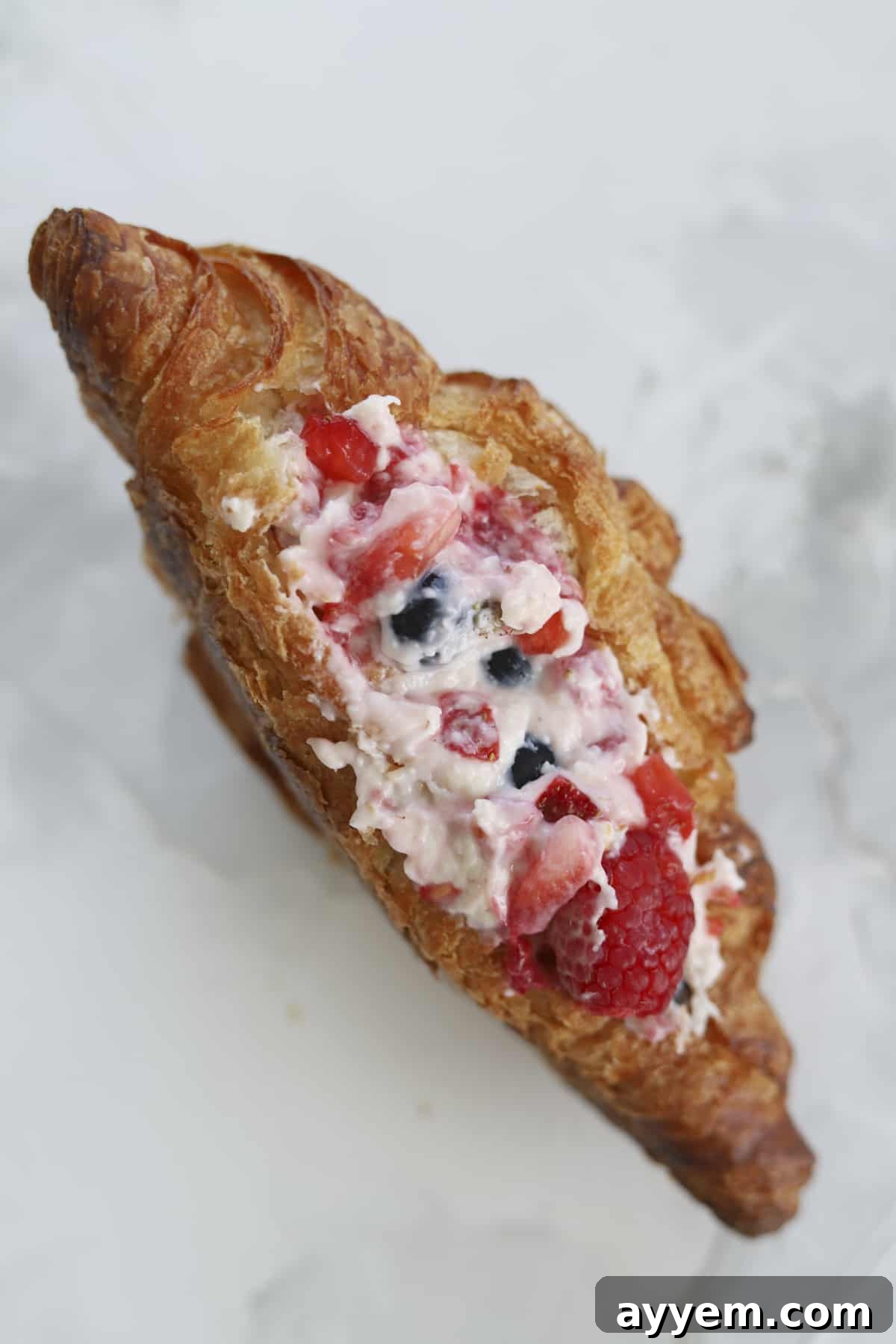 Overhead shot of a single croissant stuffed with a vibrant berry and cream cheese filling.