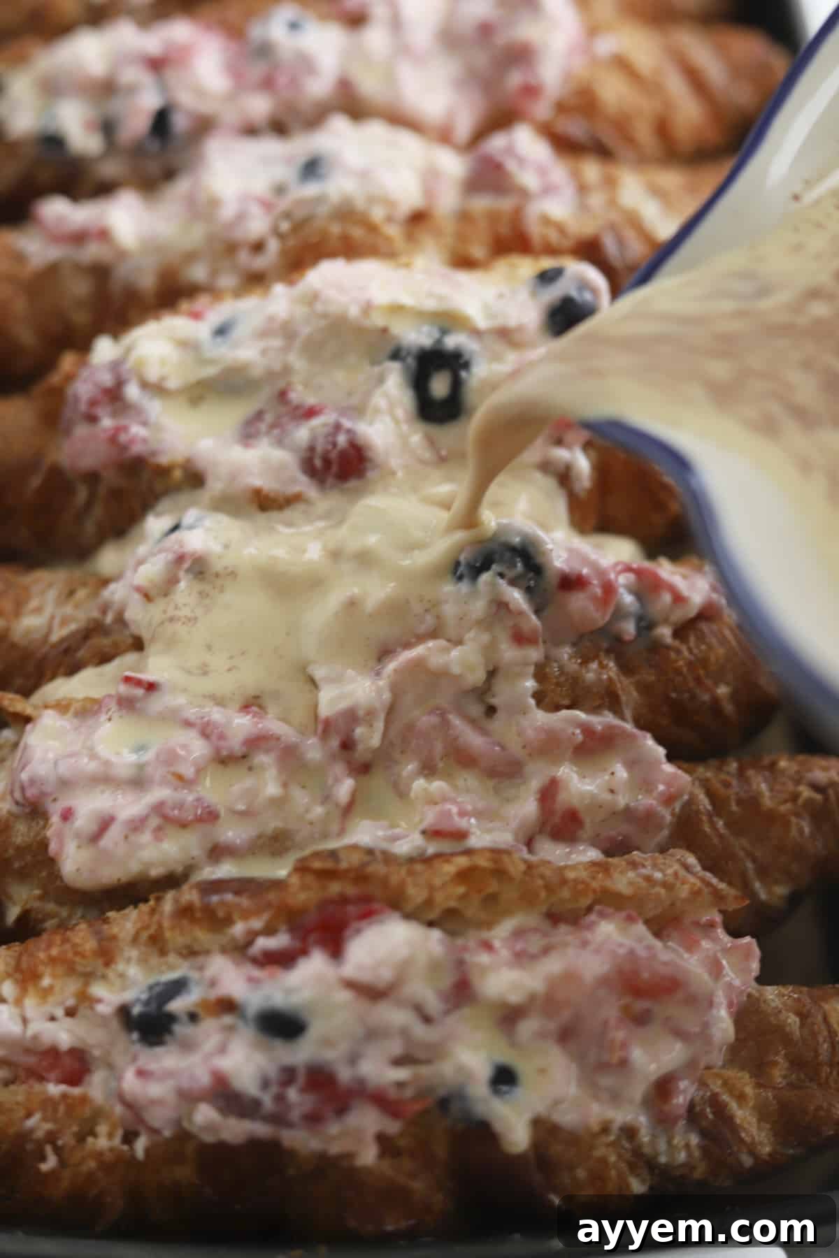 Side view of croissants in a baking dish, being drizzled with the French toast custard.