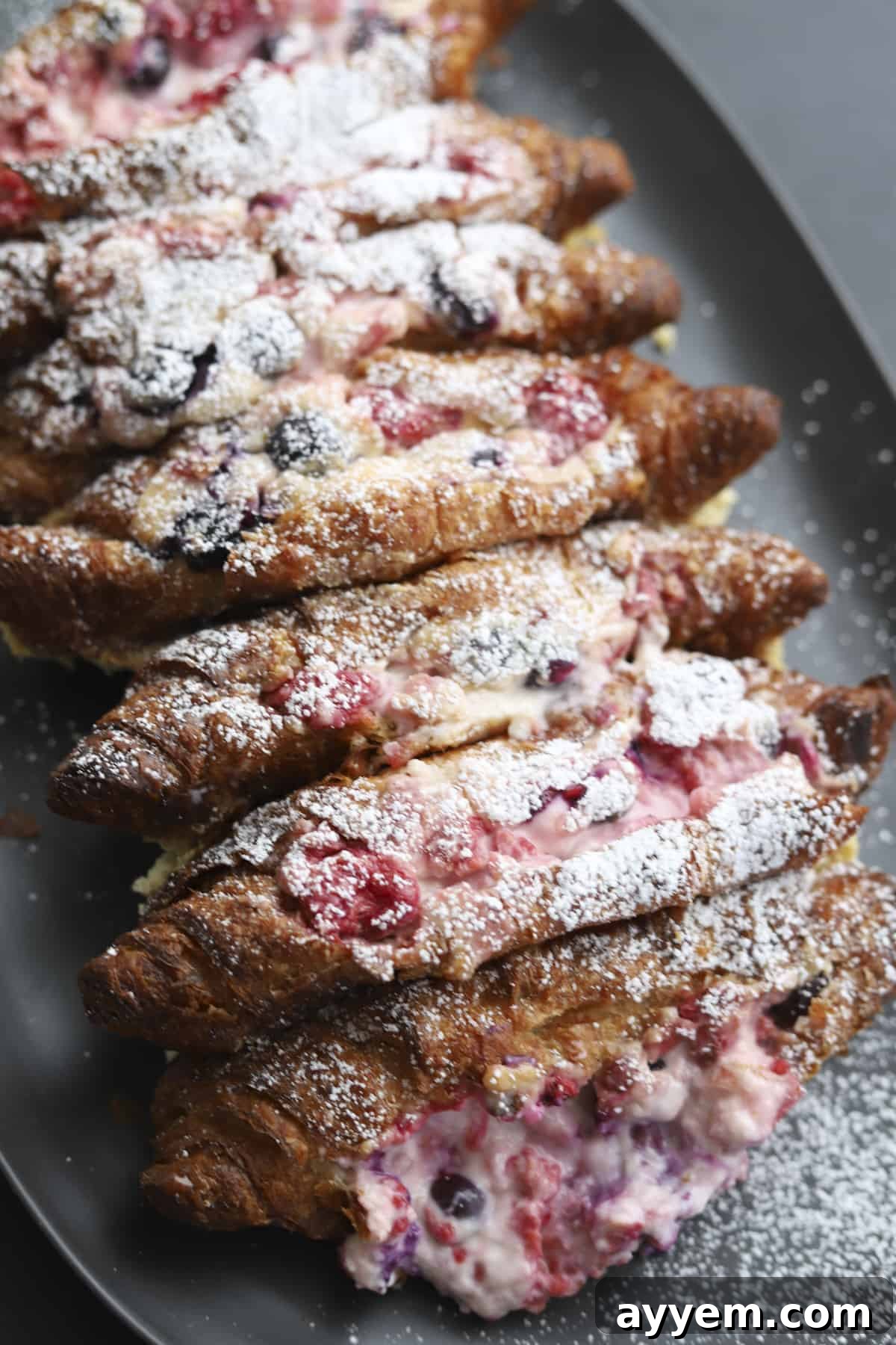 Overhead shot of the Berry Stuffed Croissant French Toast Bake on a serving platter, lightly dusted with powdered sugar and surrounded by fresh berries.