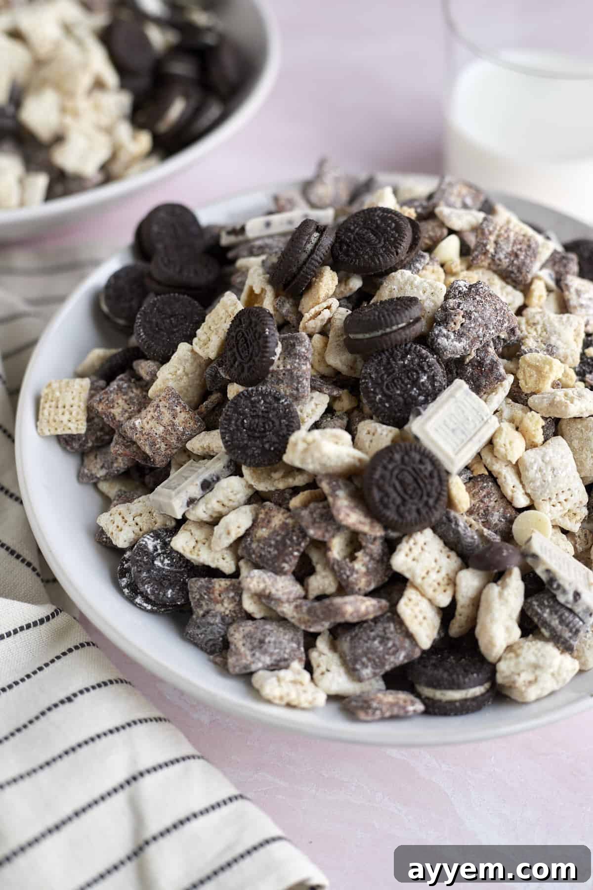 A bowl filled with irresistible cookies and cream muddy buddies, featuring crumbled Oreos and a dusting of powdered sugar.