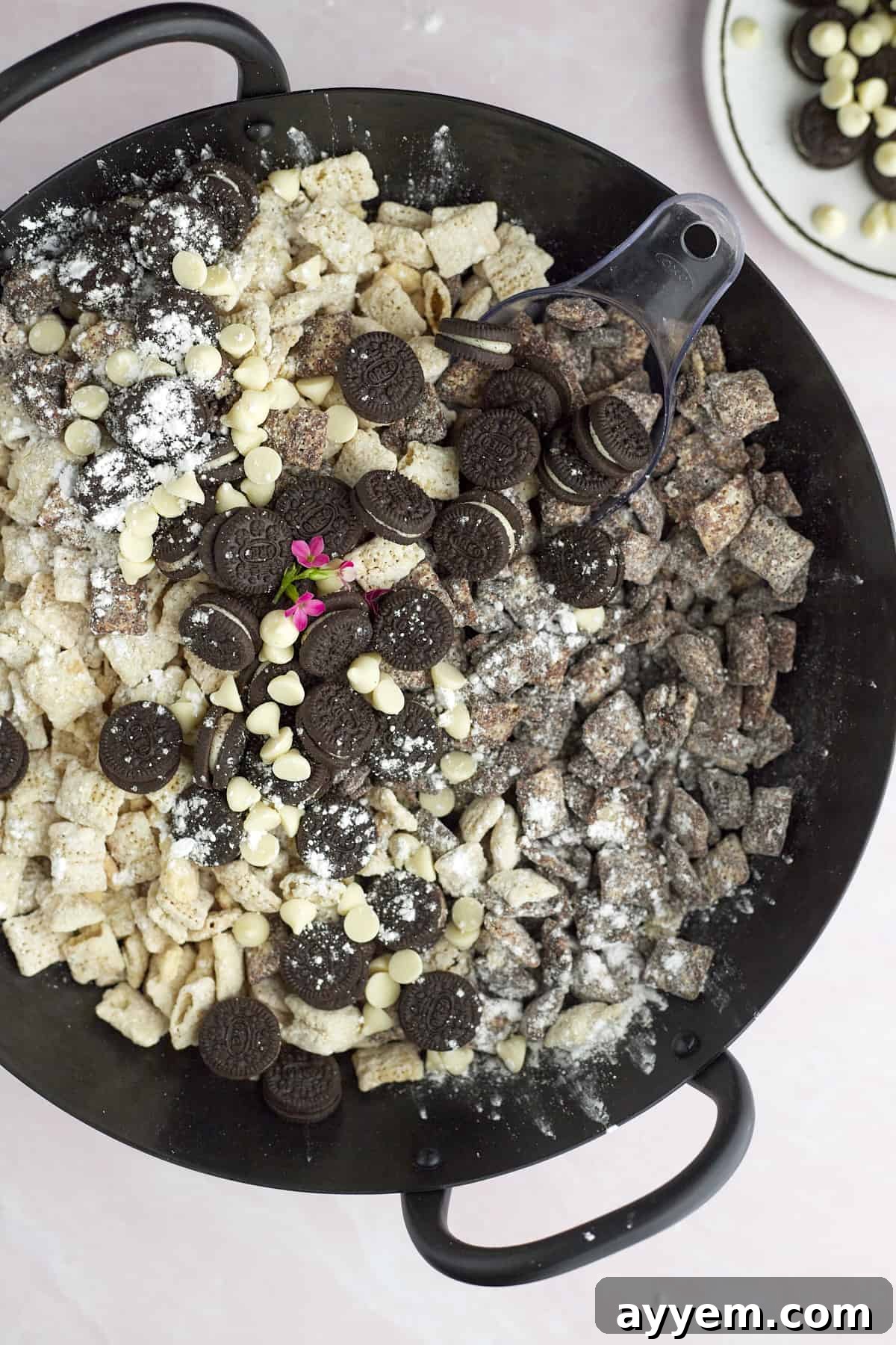 A close-up shot of cookies and cream muddy buddies, adorned with mini Oreos and white chocolate chips, in a rustic skillet.