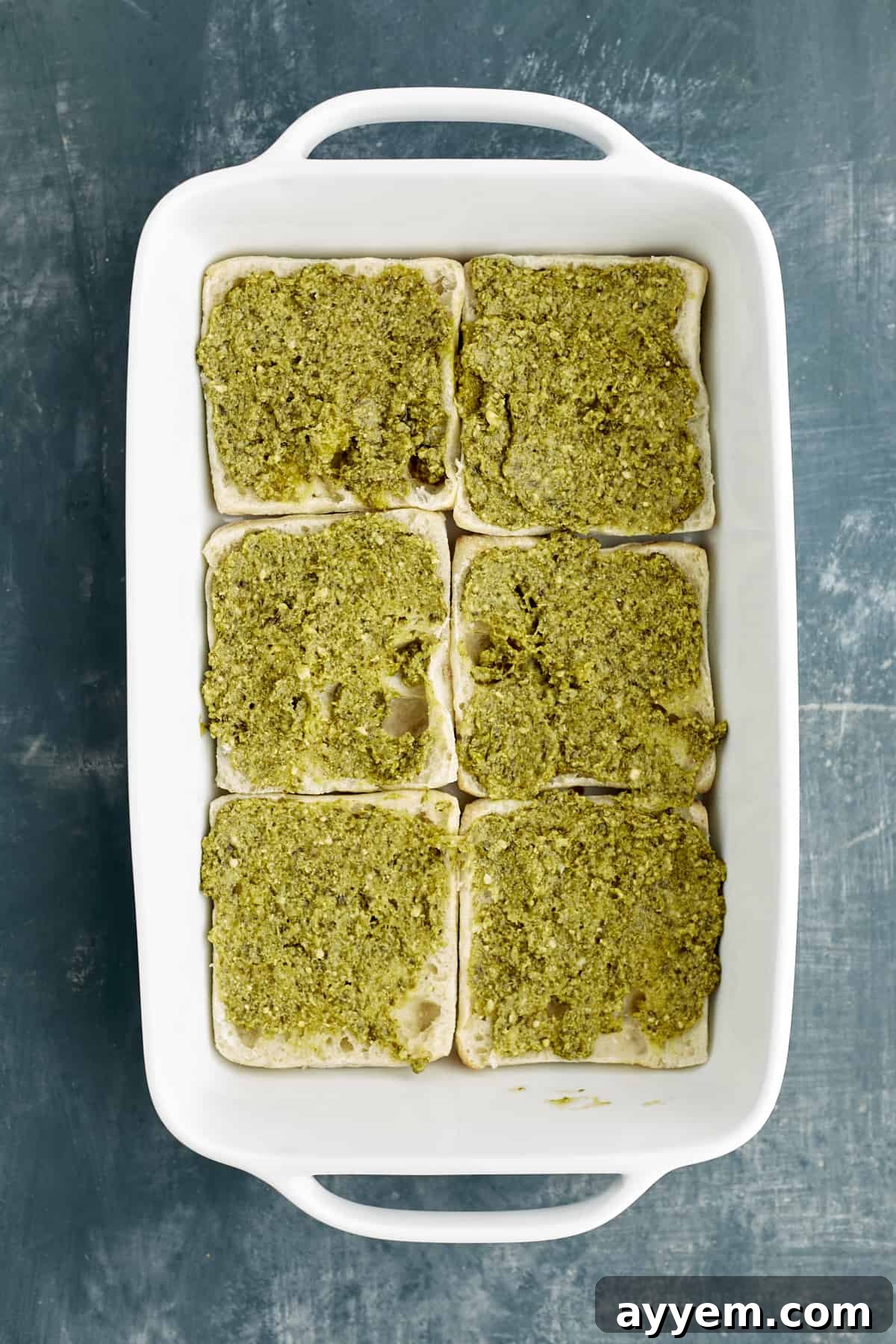 Fresh Turkey Caprese Sandwich 4 Sliced ciabatta bread in a baking dish, generously topped with fresh basil pesto.