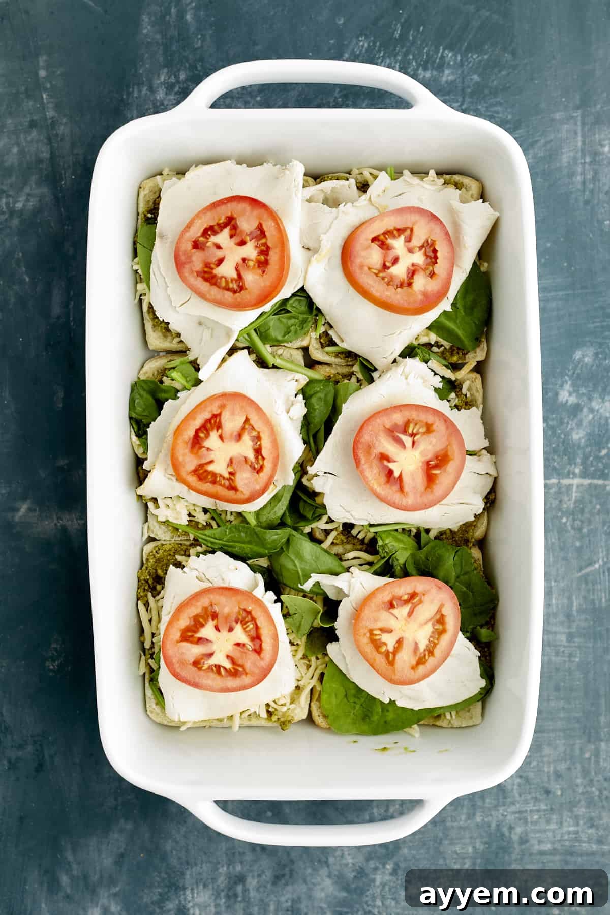 Fresh Turkey Caprese Sandwich 7 Ciabatta buns in a baking dish, expertly layered with pesto, spinach, turkey, and ripe tomato slices.