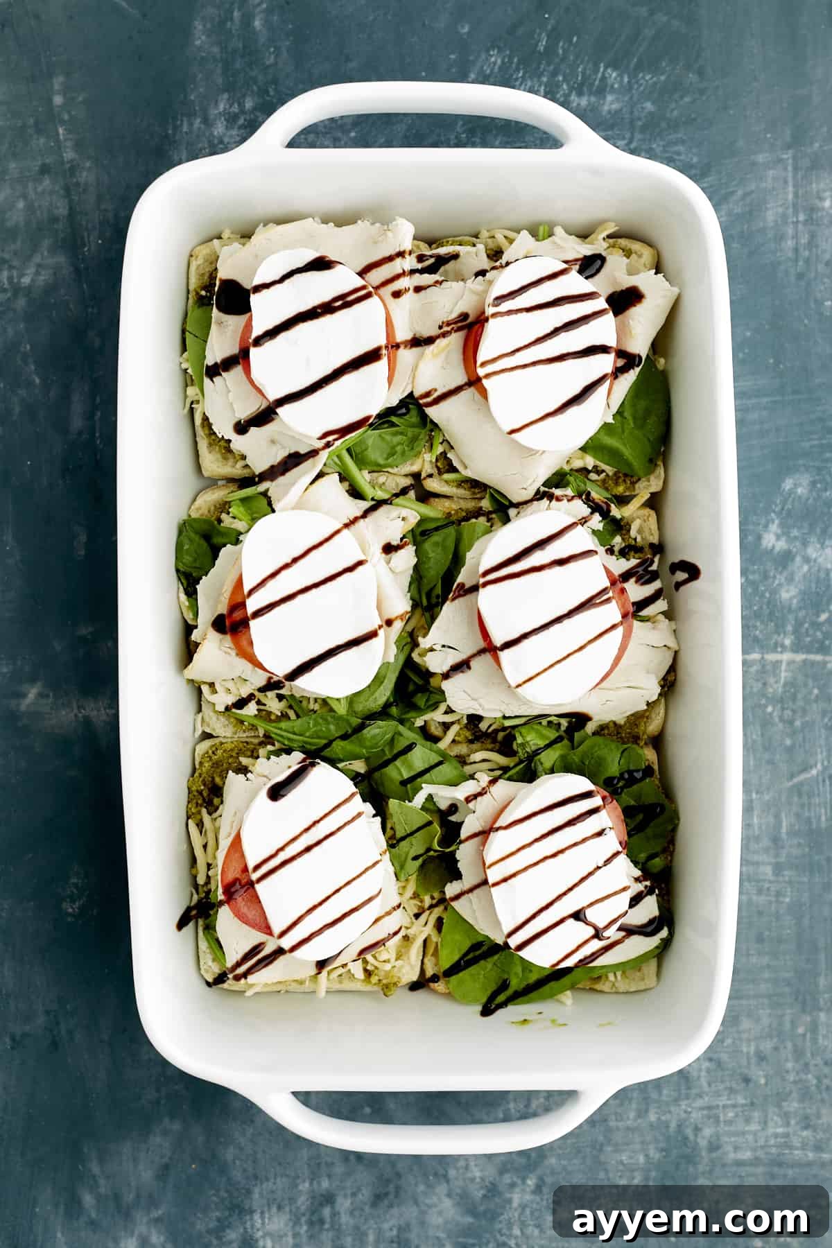Fresh Turkey Caprese Sandwich 9 Sliced ciabatta buns in a white baking dish, topped with generous layers of pesto, spinach, turkey, tomatoes, mozzarella, and a glistening balsamic glaze.