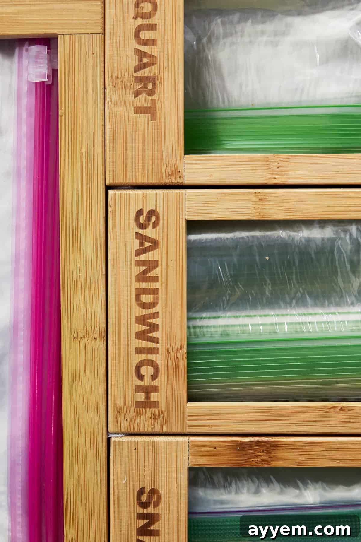 A neatly organized kitchen drawer featuring a one-piece Ziploc bag organizer made of bamboo, with designated slots for gallon, quart, sandwich, and snack bags.
