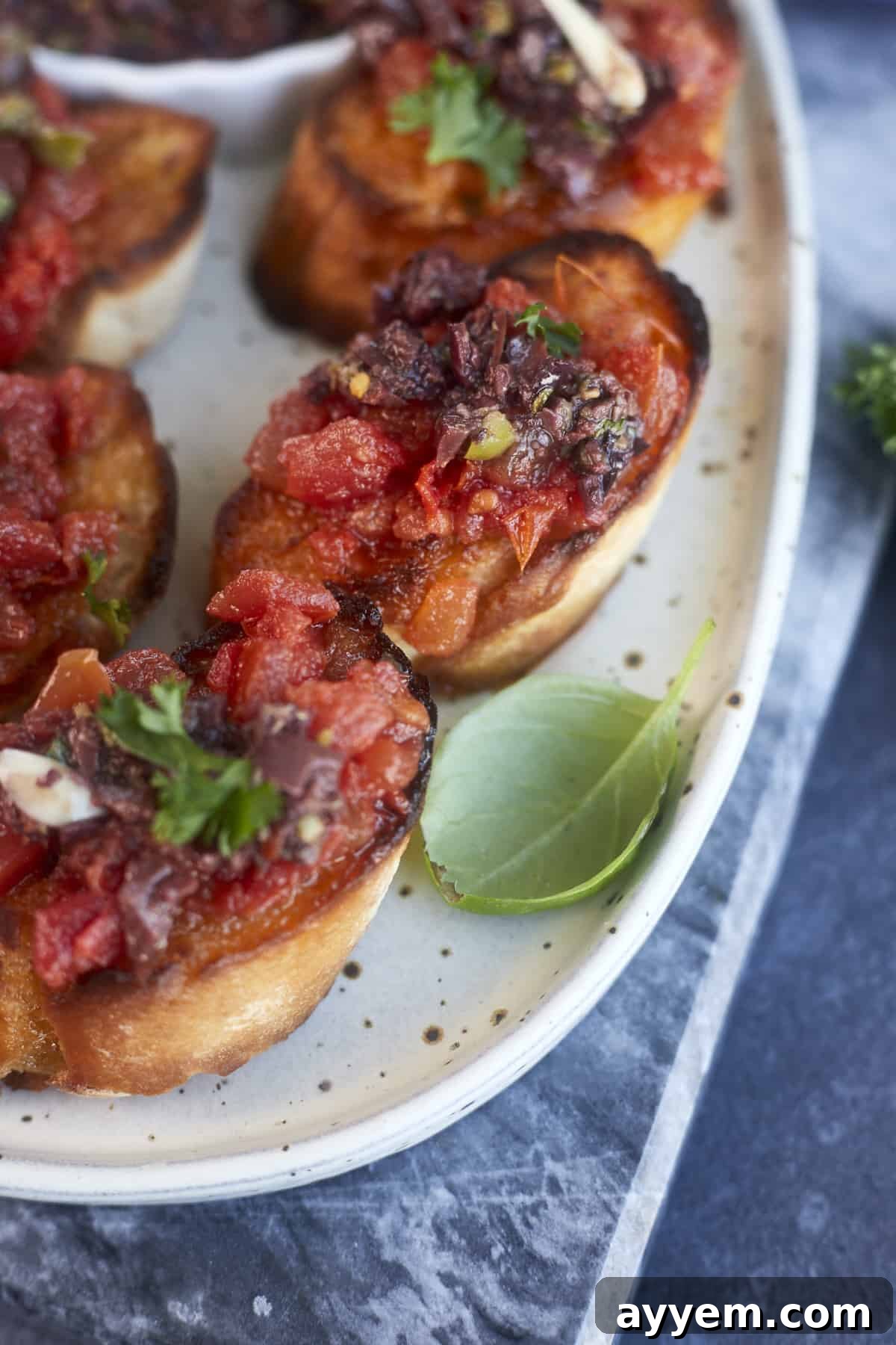Close-up of perfectly assembled Olive Tapenade Bruschetta on a white plate, ready to be enjoyed.