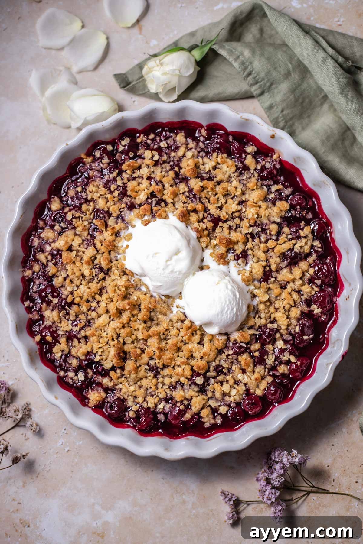 Warm cherry crisp topped with two generous scoops of creamy vanilla ice cream, served in a rustic dish, highlighting the bubbly fruit filling and golden-brown oat topping.