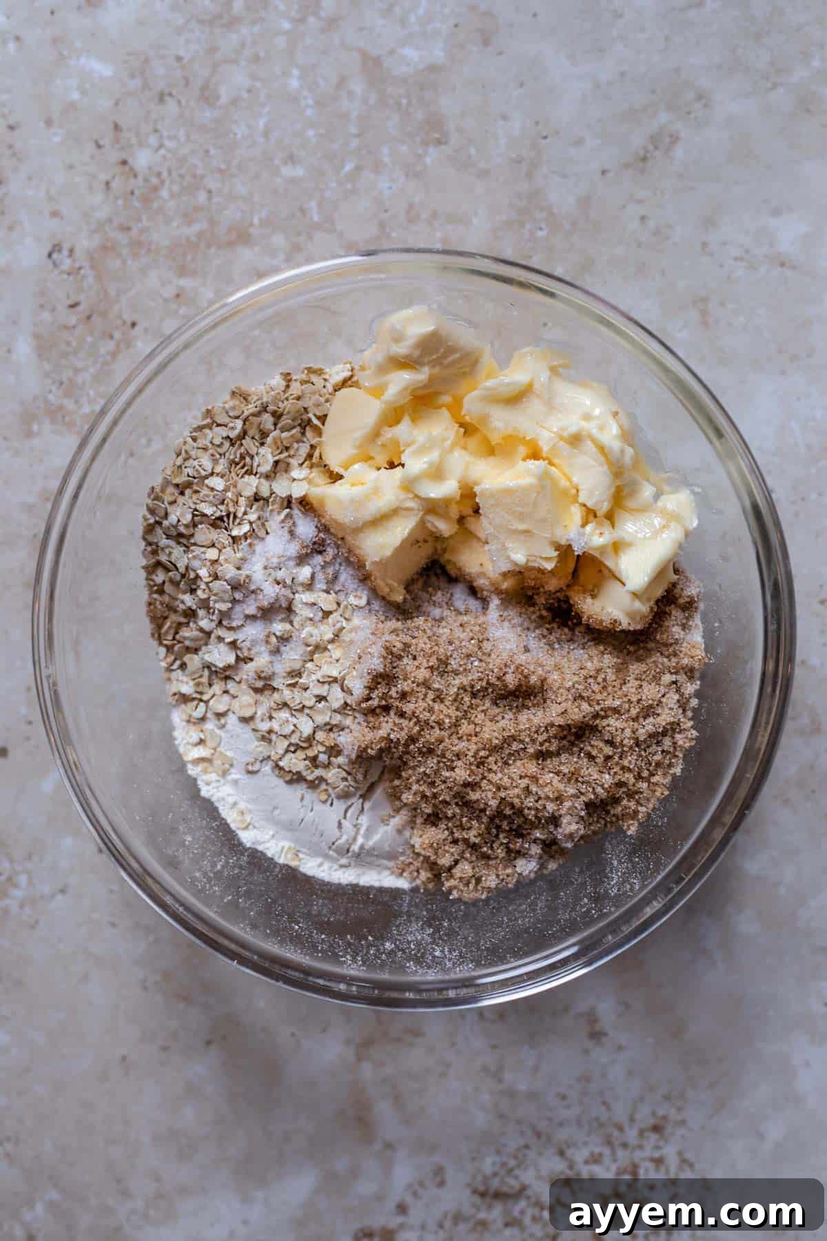 A mixing bowl filled with dry ingredients for the crisp topping: flour, rolled oats, brown sugar, and salt, waiting for butter.