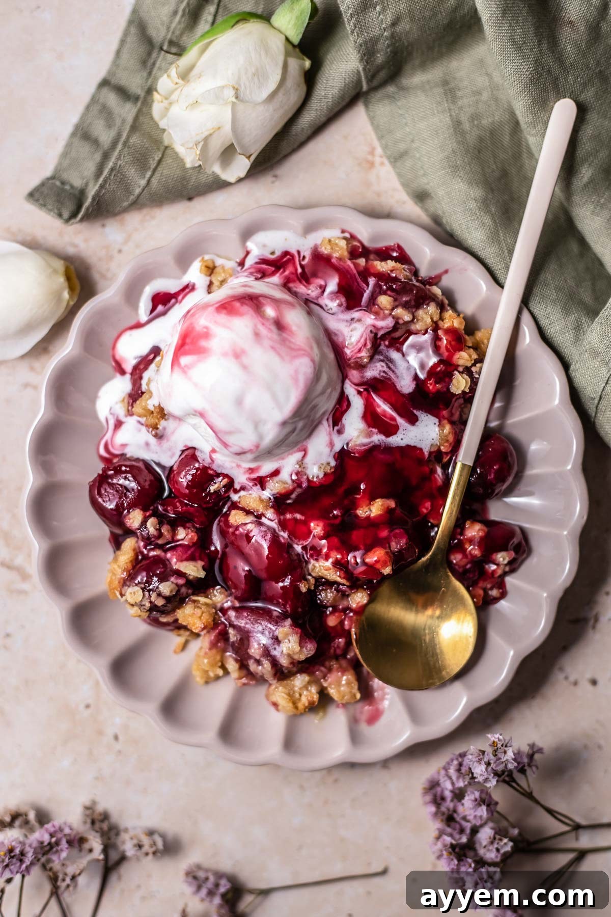 A close-up shot of a single serving of cherry crisp, topped with melted vanilla ice cream, with a spoon digging in to reveal the juicy cherries and crumbly oat topping.