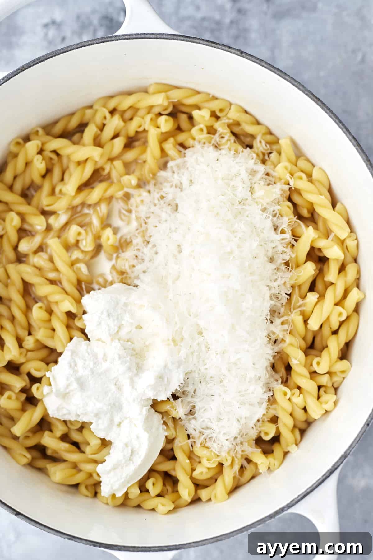 Creamy Lemon Ricotta One-Pot Delight 5 pasta noodles topped with Parmesan cheese and heavy cream, showing the rich sauce developing