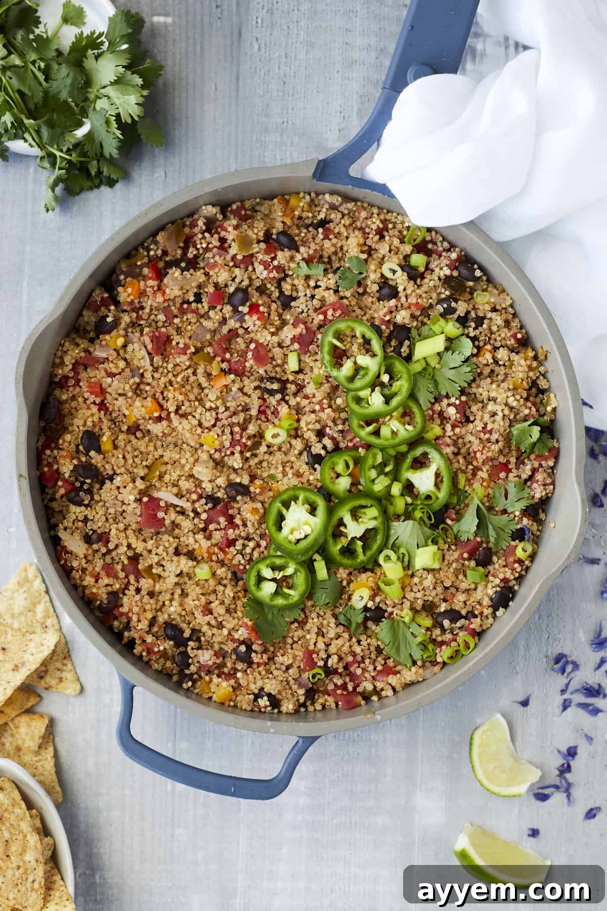 overhead image of a large pot full of Mexican quinoa with veggies and beans topped with sliced jalapenos and cilantro