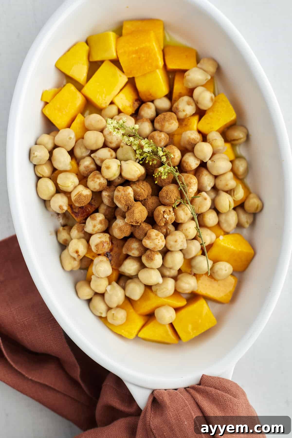 Cubed butternut squash and chickpeas in an oval baking dish, seasoned with cinnamon and ready for roasting.