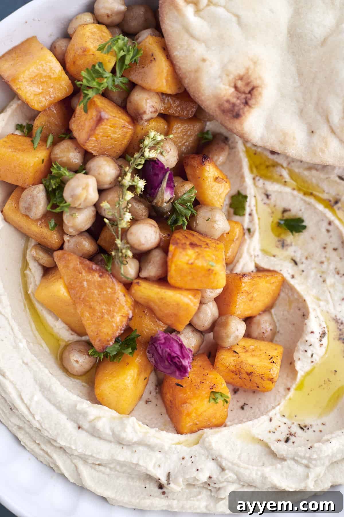 Close-up image of cinnamon-roasted chickpeas and butternut squash over a bed of roasted maple butternut squash hummus, garnished with herbs.