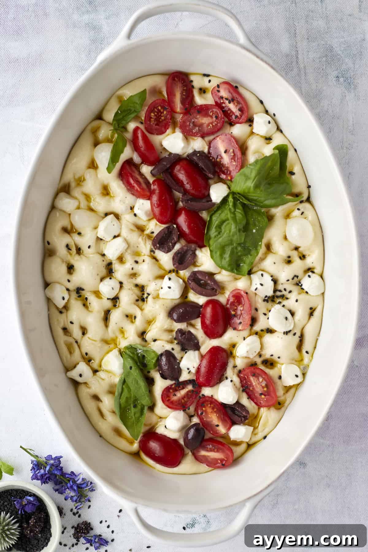 unbaked no knead focaccia bread topped with tomatoes, olives, fresh herbs, and mozzarella 