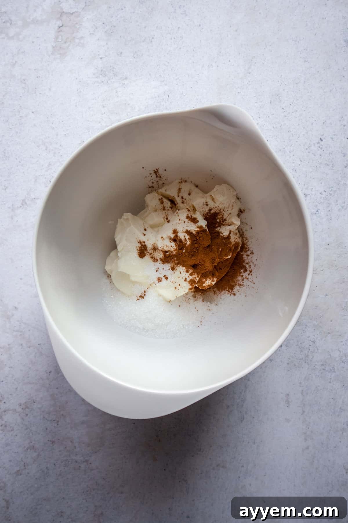 A bowl containing softened cream cheese, granulated sugar, and ground cinnamon, ready to be mixed for the filling.