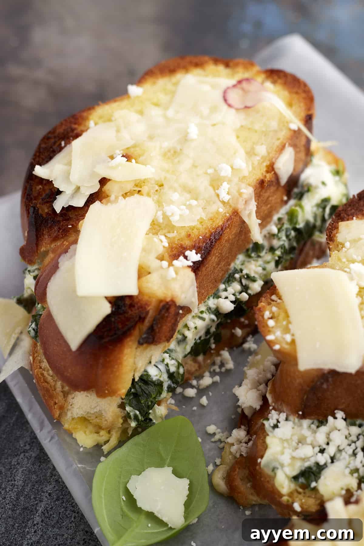 A close-up, mouth-watering image of a sliced Spanakopita-Inspired Spinach Grilled Cheese, revealing layers of creamy spinach, melted mozzarella, and feta cheese between perfectly toasted bread, garnished with a sprig of fresh dill.
