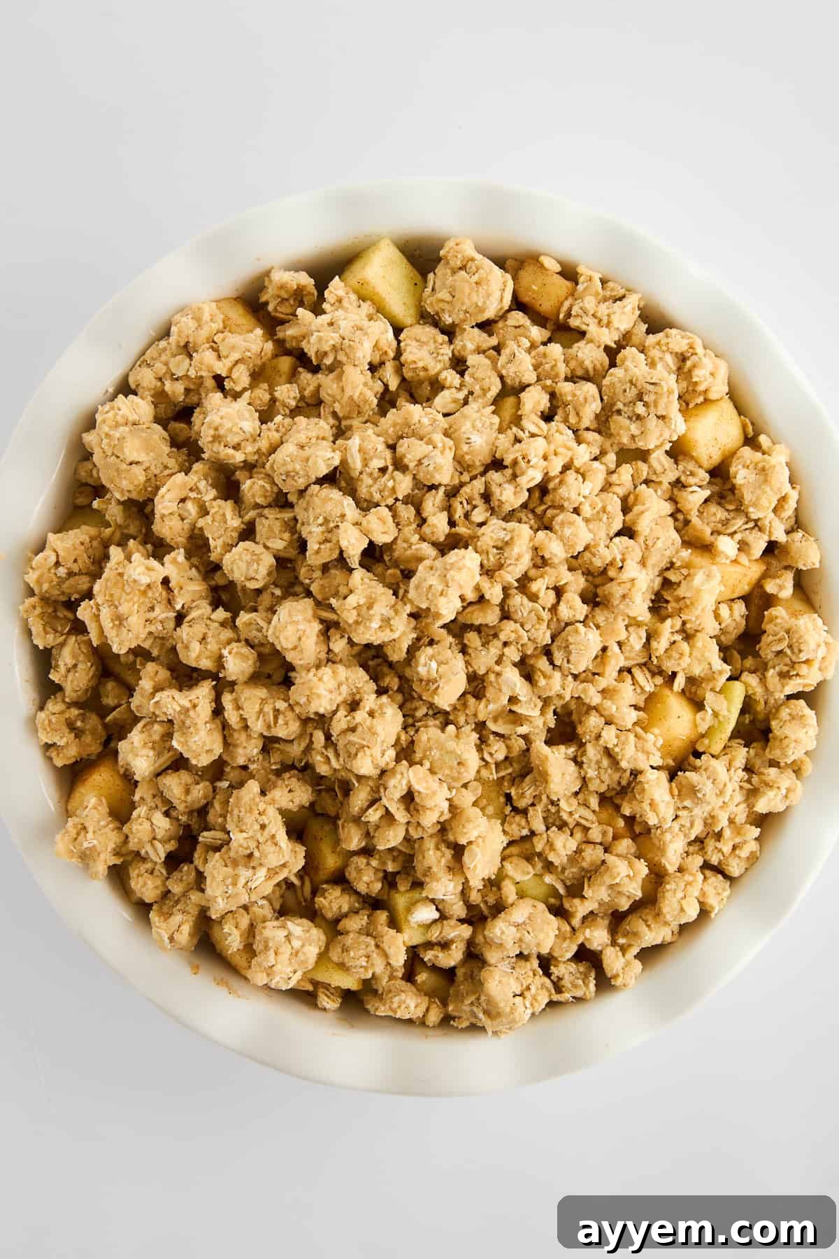 An unbaked apple crisp, showing the apple filling covered with the generous oat topping in a baking dish.