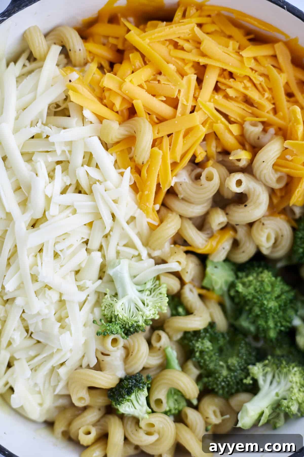 Close-up shot of cavatappi noodles, vibrant green broccoli florets, and melting Mozzarella and Cheddar cheese in a pot, showcasing the rich texture.