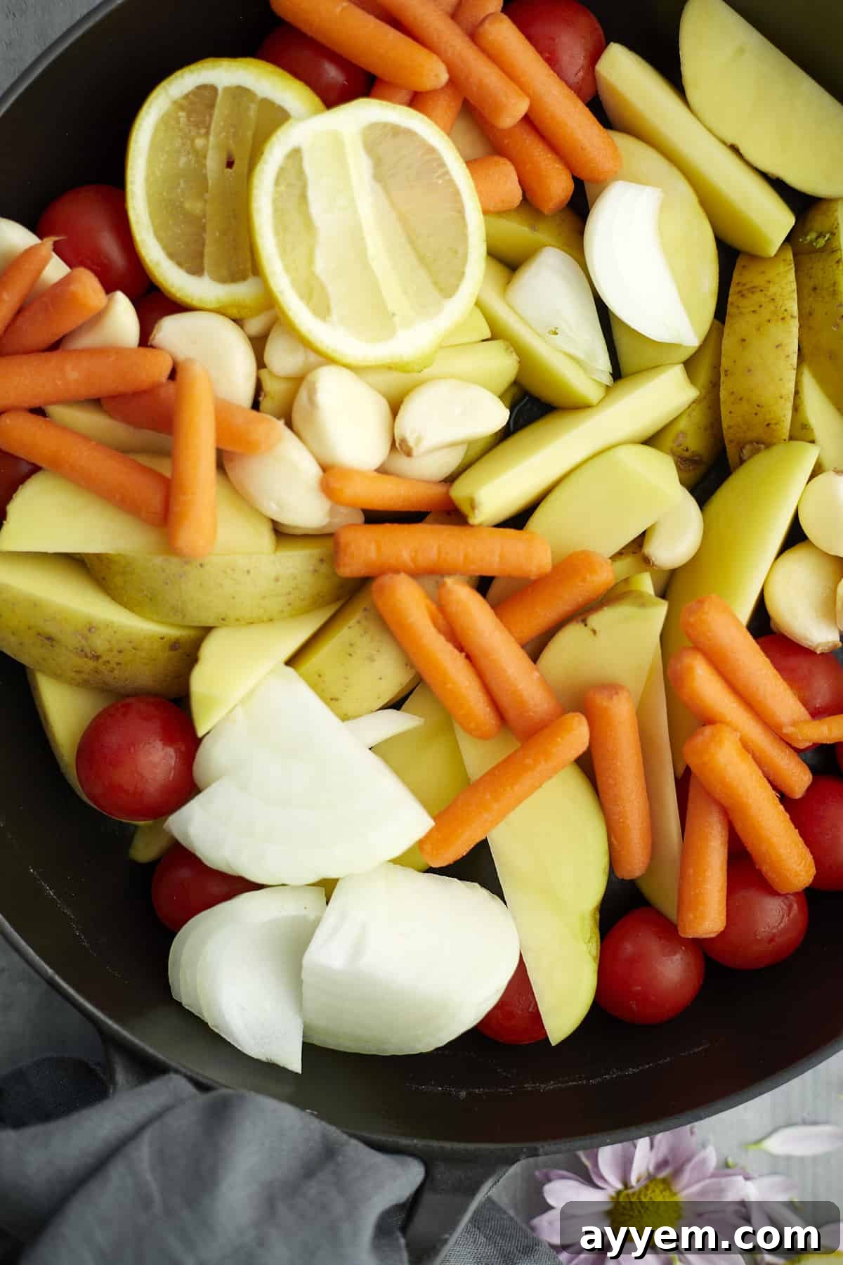 Overhead view of fresh potatoes, carrots, onions, tomatoes, garlic, and lemon ready for roasting in a pan.