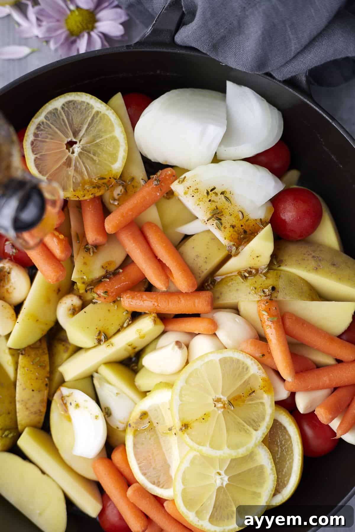 Overhead image of marinated potatoes, onions, carrots, and tomatoes topped with lemon slices in a pan, ready for roasting.