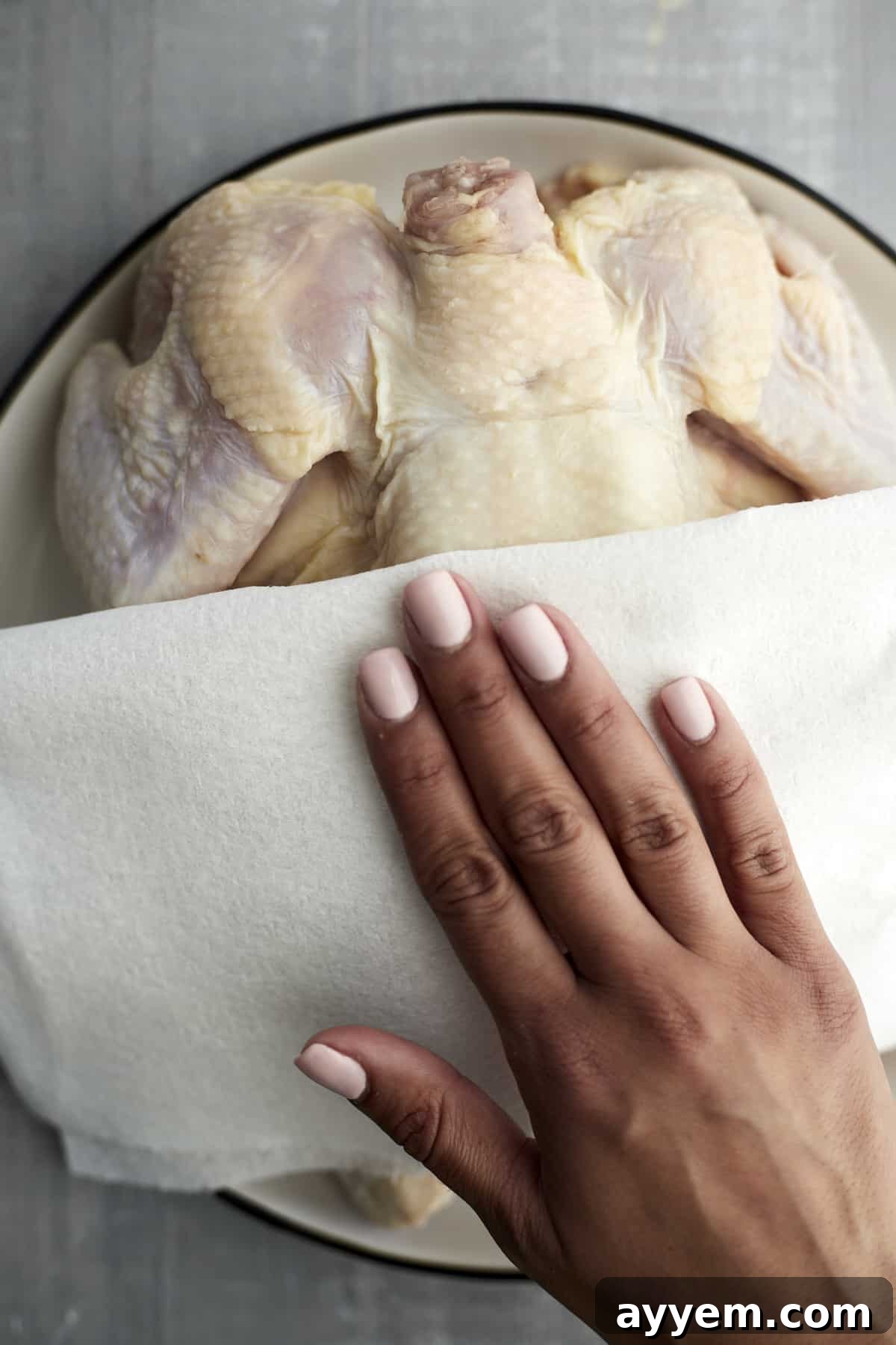 A hand using a paper towel to pat a whole raw chicken dry before seasoning and roasting.