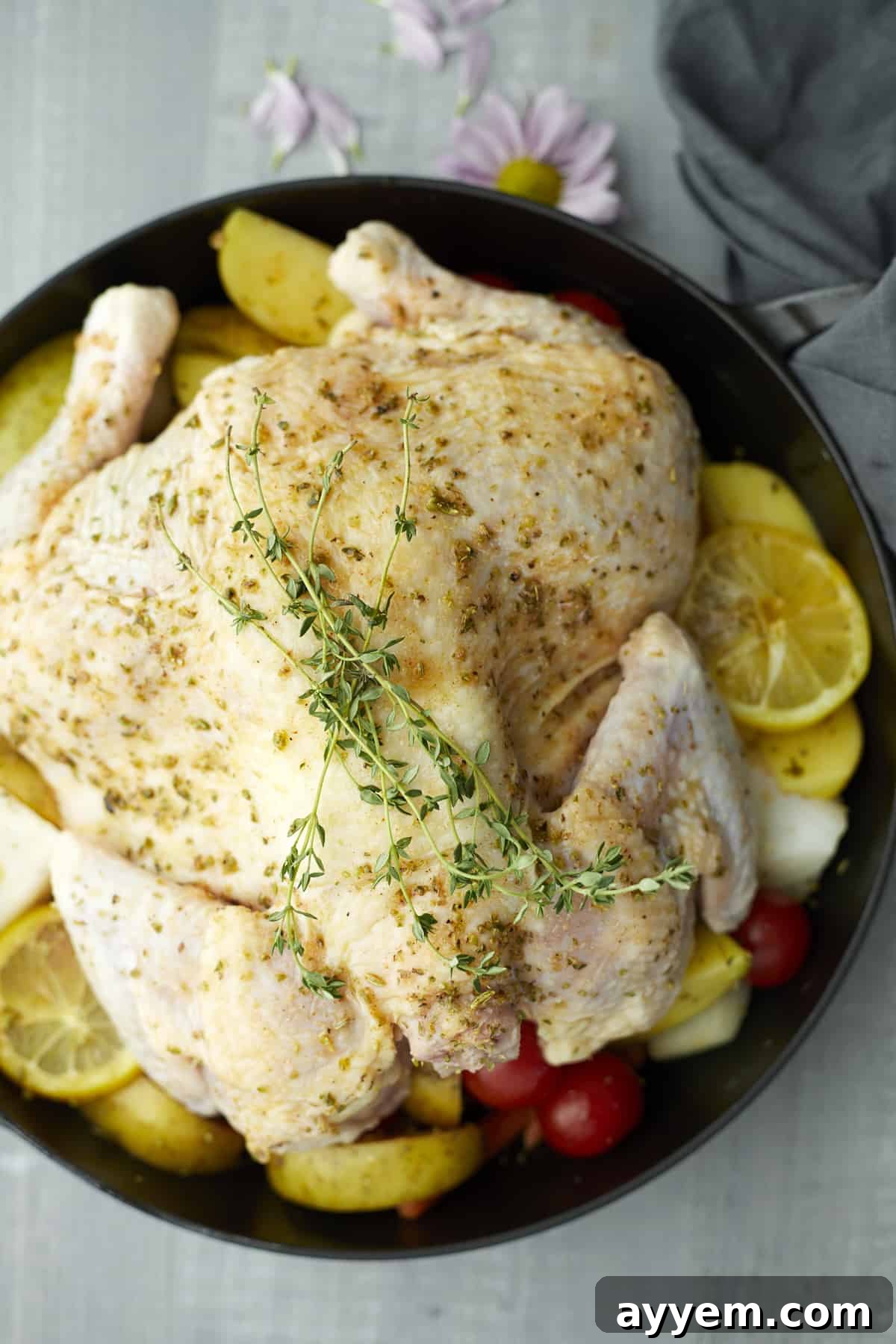 Raw whole butterflied chicken seasoned and laid over a bed of mixed vegetables on a plate, ready for the oven.