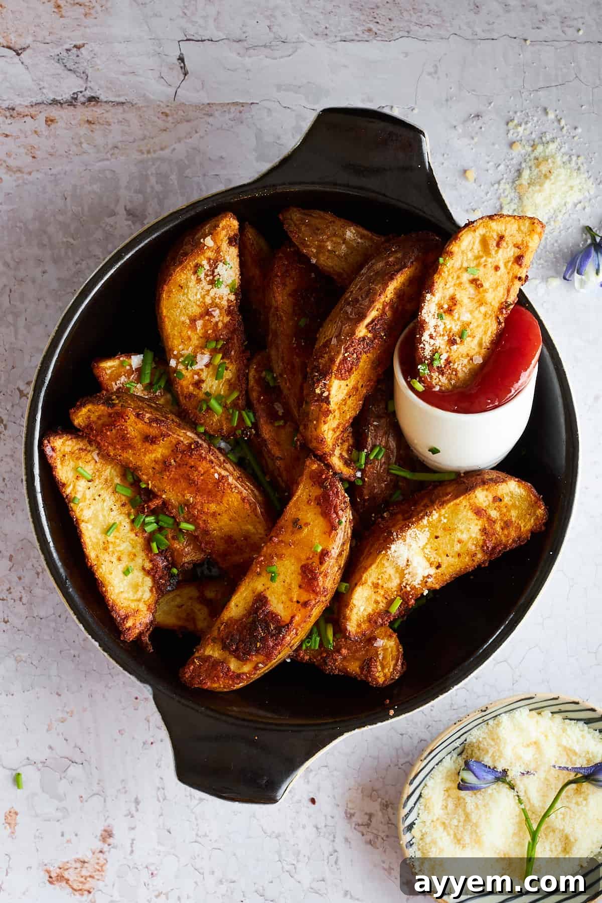 A bowl of golden-brown garlic Parmesan potato wedges, perfectly crispy, with a side of ketchup for dipping.