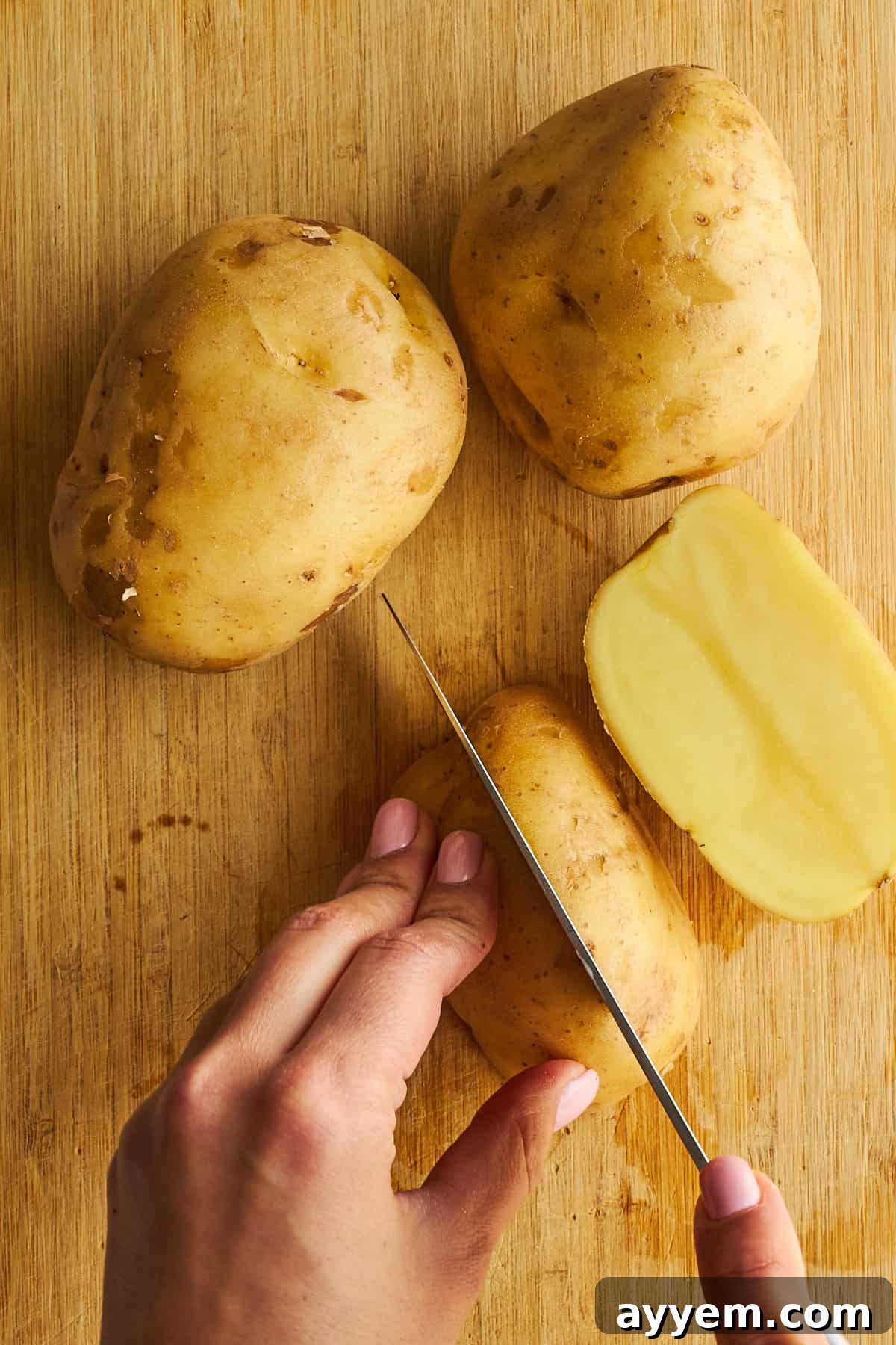 Potatoes being carefully sliced into consistent wedges on a cutting board.
