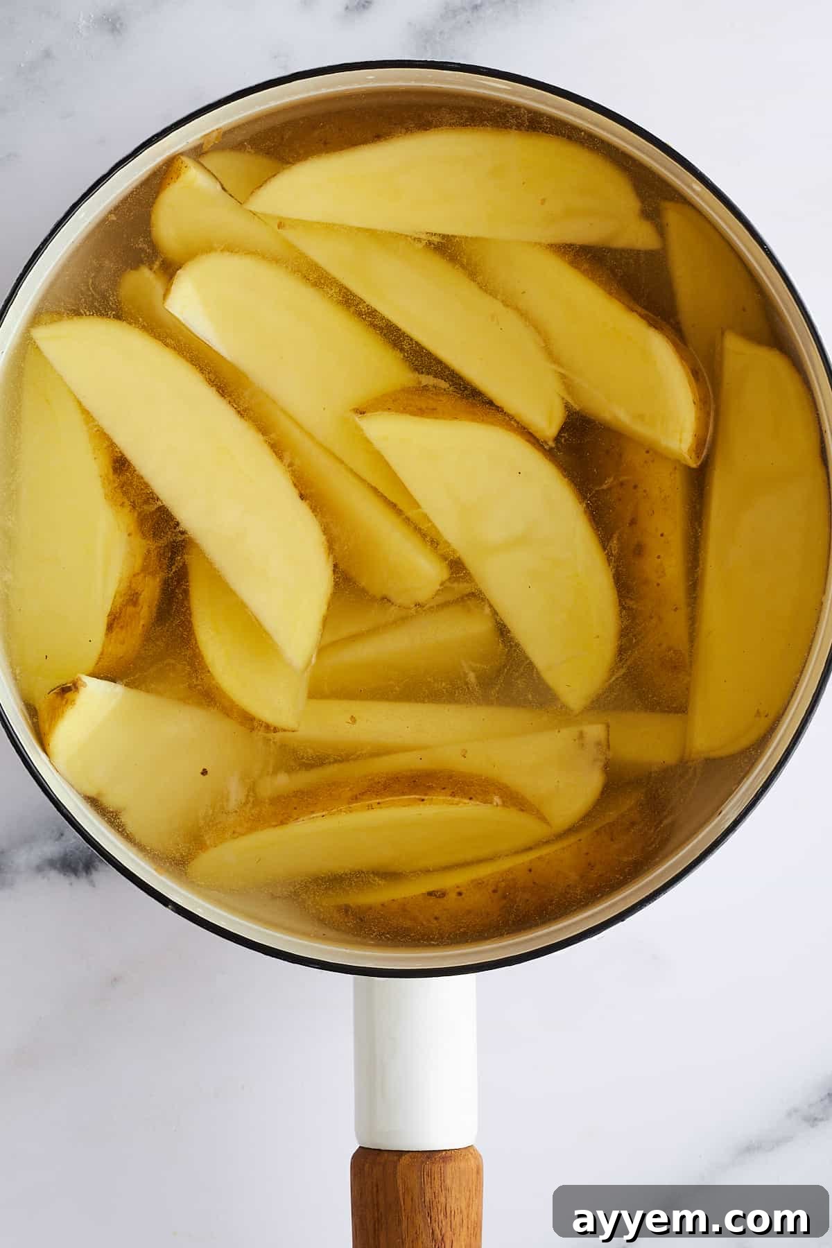 Potato wedges submerged in a pot of simmering water on a stovetop, preparing for par-boiling.