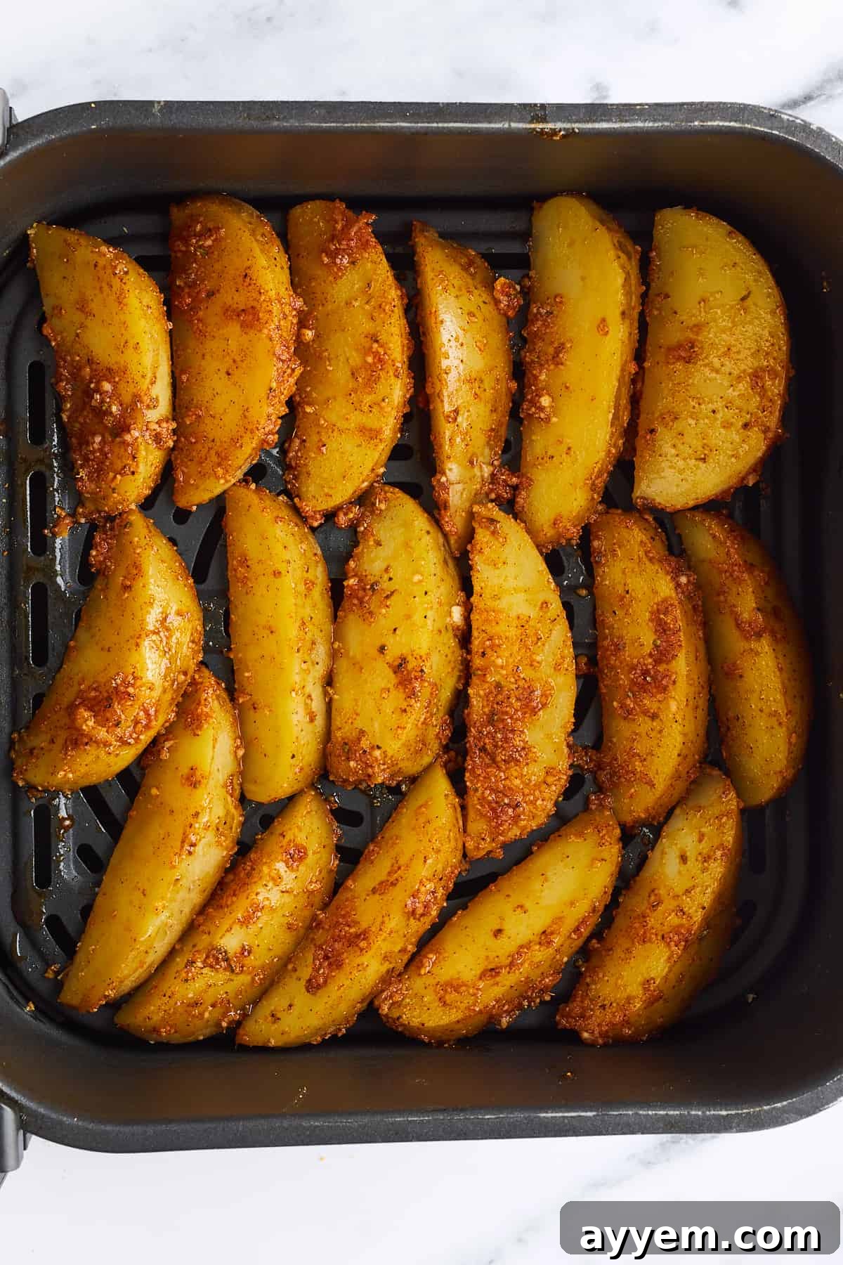 Seasoned, unbaked garlic Parmesan potato wedges neatly arranged in a single layer within an air fryer basket, ready for cooking.