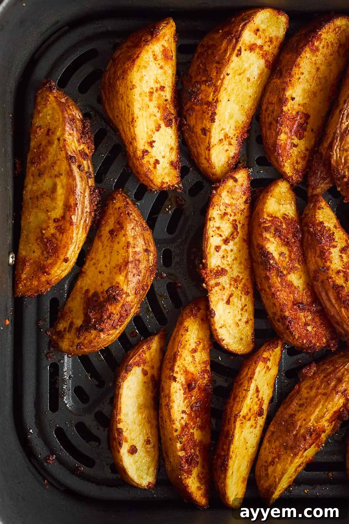 Perfectly cooked, golden-brown garlic Parmesan potato wedges filling an air fryer basket, looking crispy and delicious.