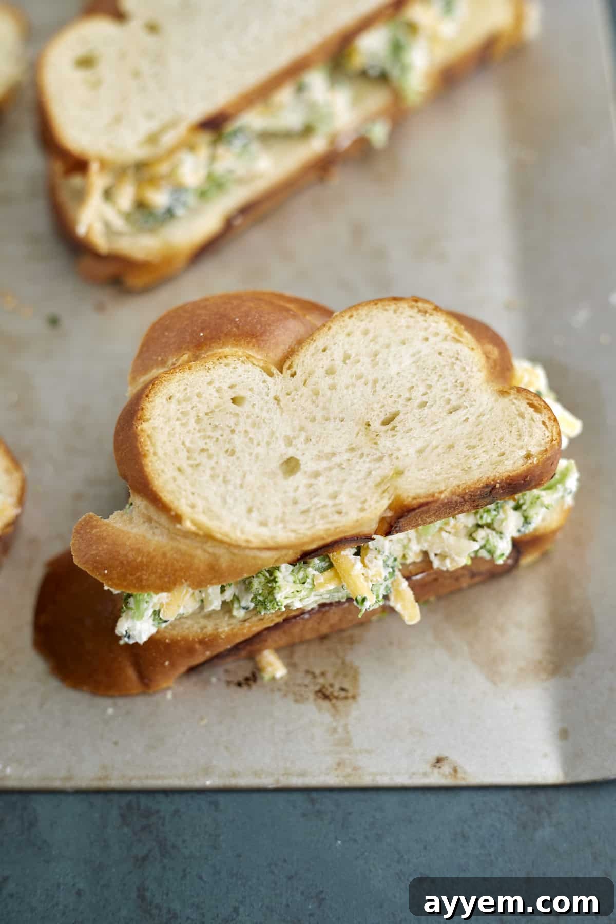 Crispy Oven-Baked Broccoli Cheddar Melts 4 Several uncooked grilled cheese sandwiches filled with broccoli and cheese mixture, neatly arranged on a baking sheet, ready for the oven.