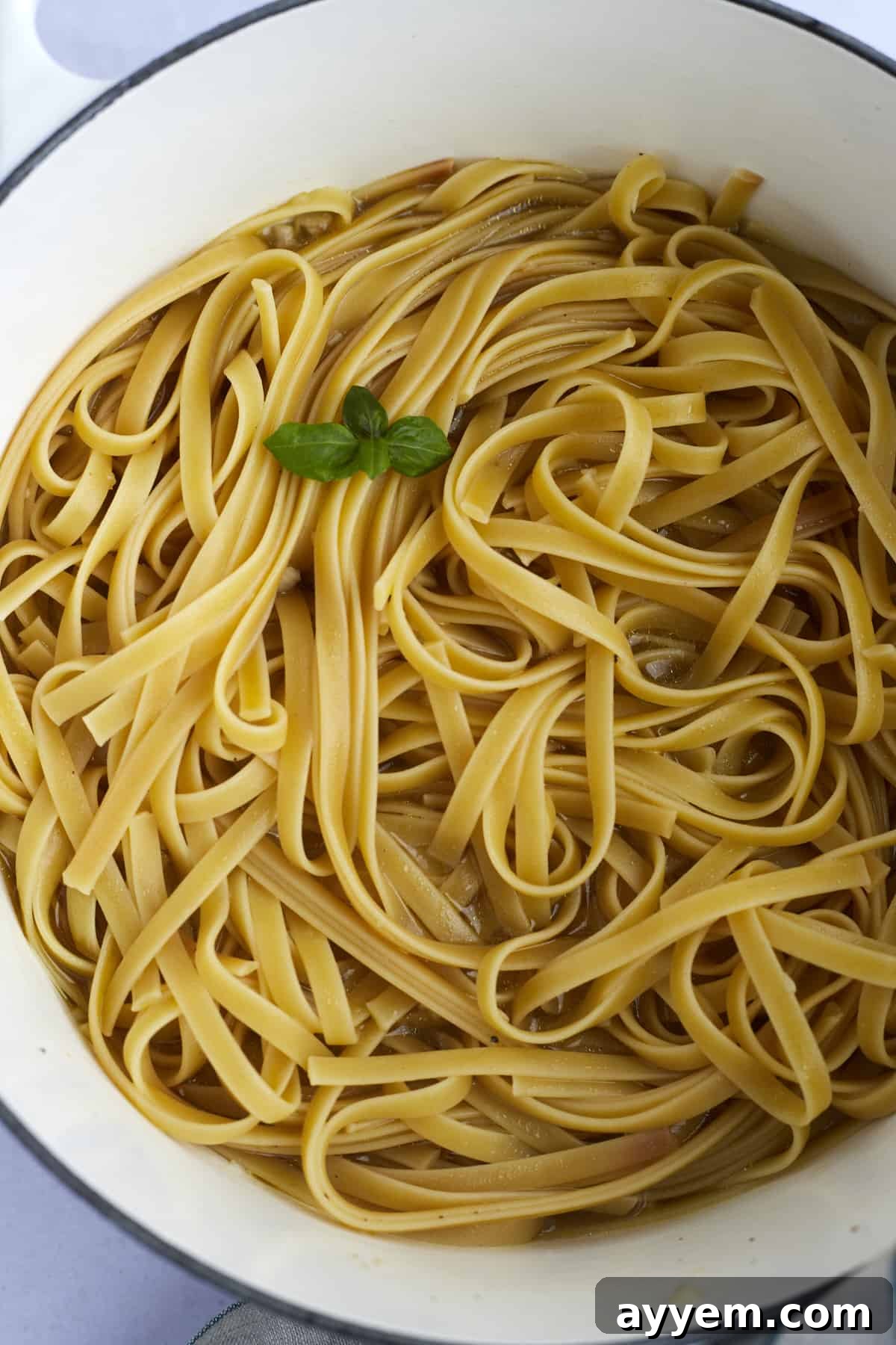 Cooked fettuccine noodles simmering gently in a flavorful broth within a single pot, absorbing all the rich liquid.