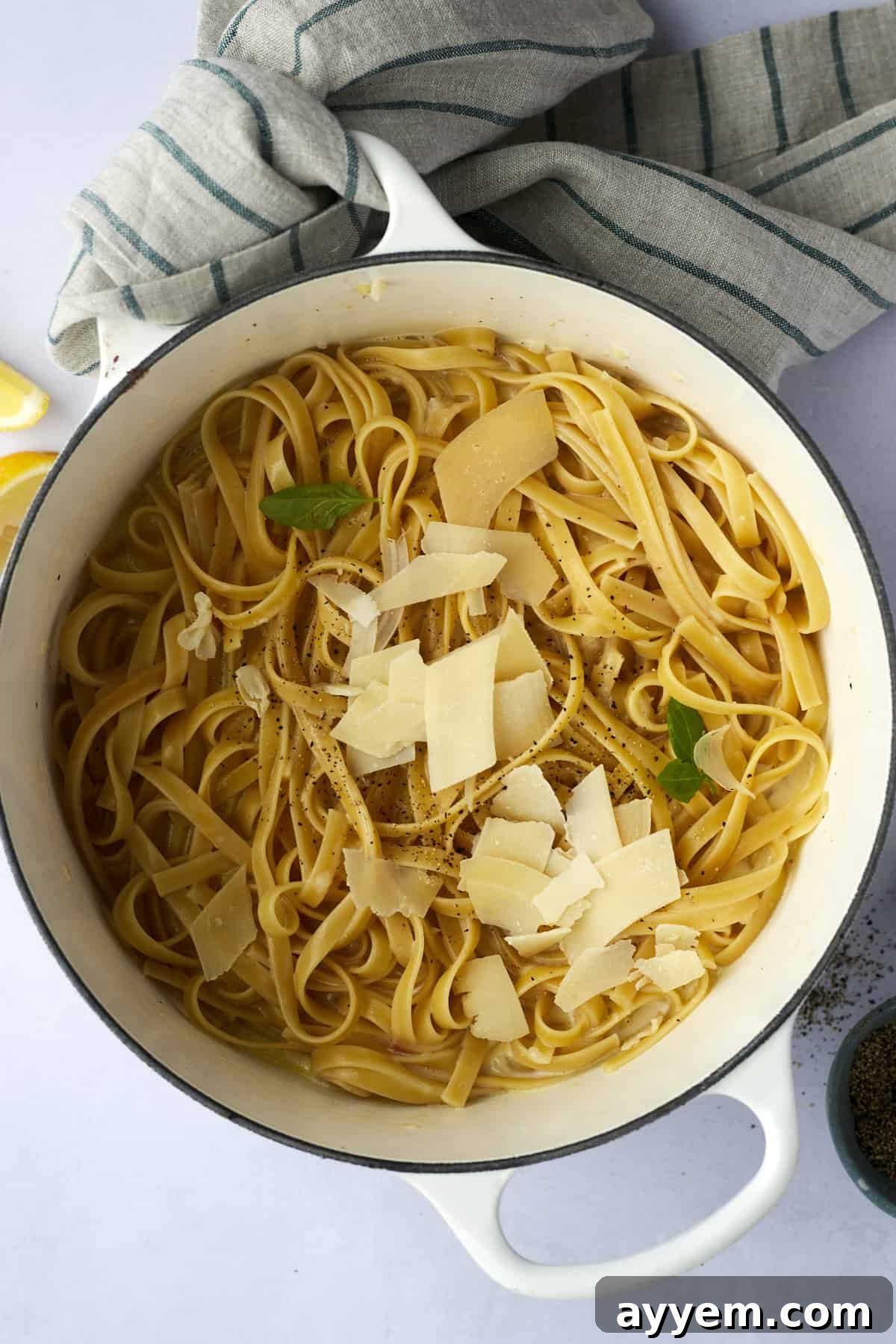 An overhead shot of a large pot filled with creamy fettuccine alfredo, generously topped with flakes of Parmesan cheese and a sprinkle of black pepper.