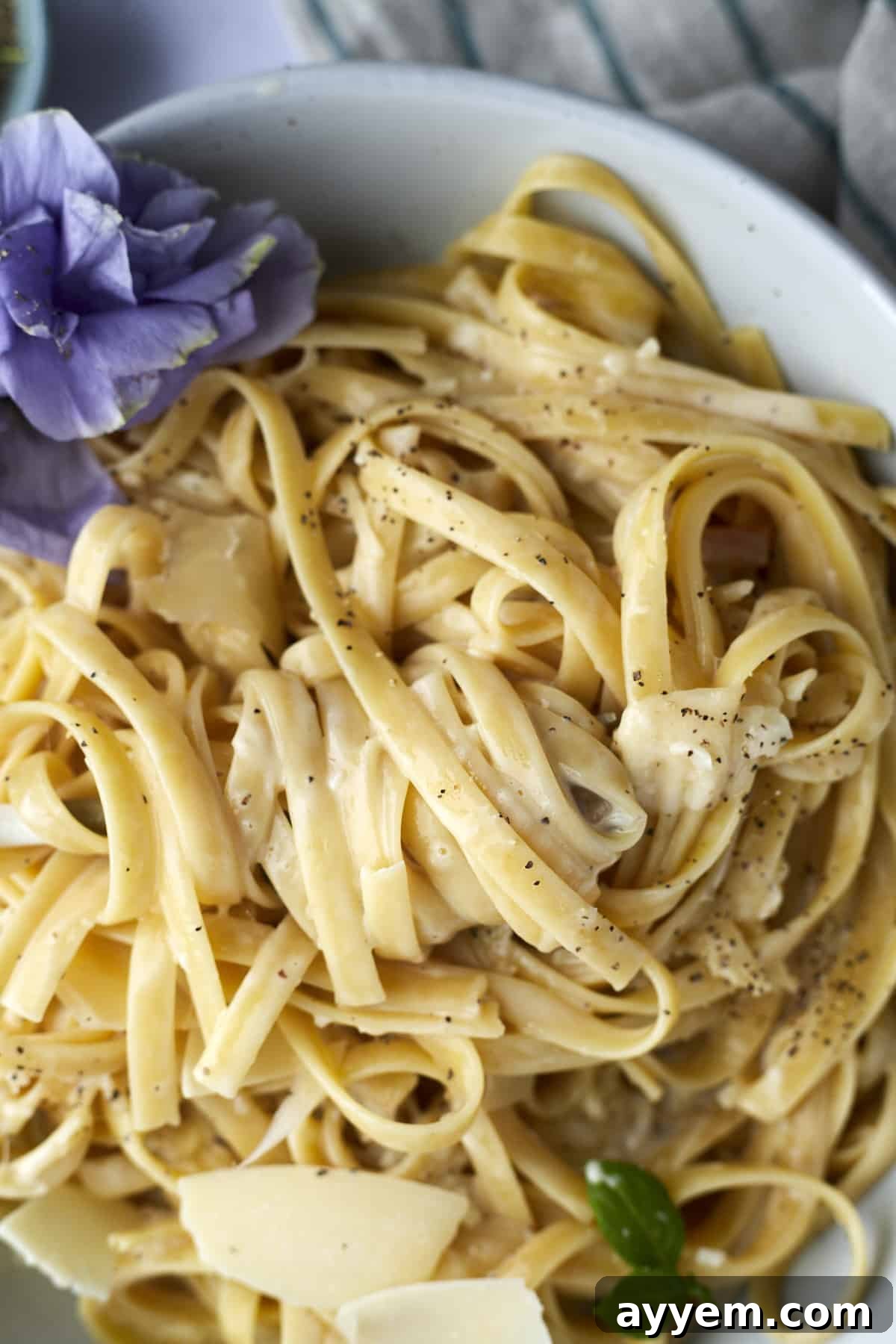 A close-up view of a bowl of one pot fettuccine alfredo, garnished with fresh herbs and a generous sprinkle of black pepper, highlighting its creamy texture.