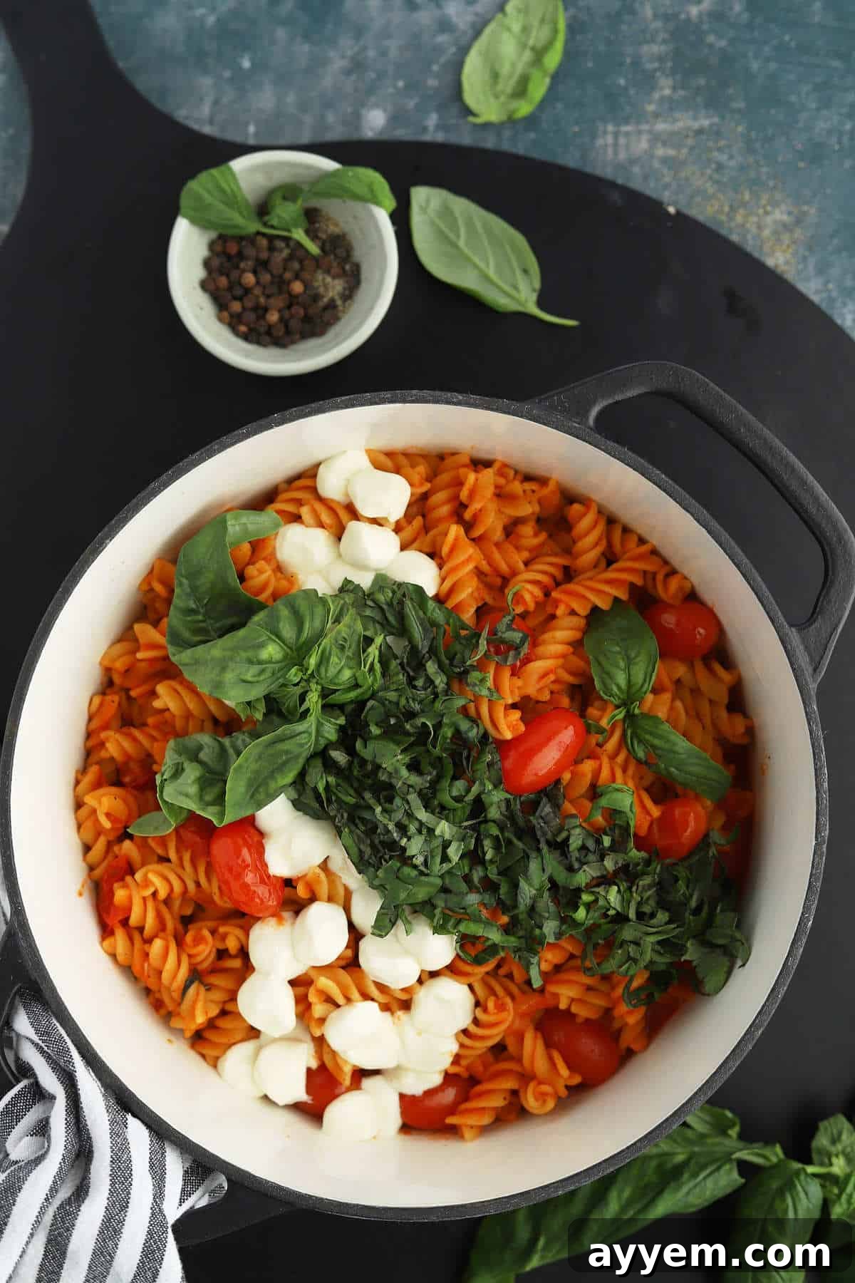 overhead image of caprese pasta in a white pot with tomatoes, basil, and mozzarella