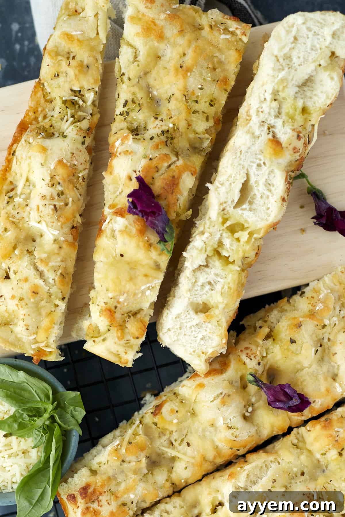 No-knead focaccia bread sliced diagonally on a cutting board, showcasing its golden crust and cheesy interior.
