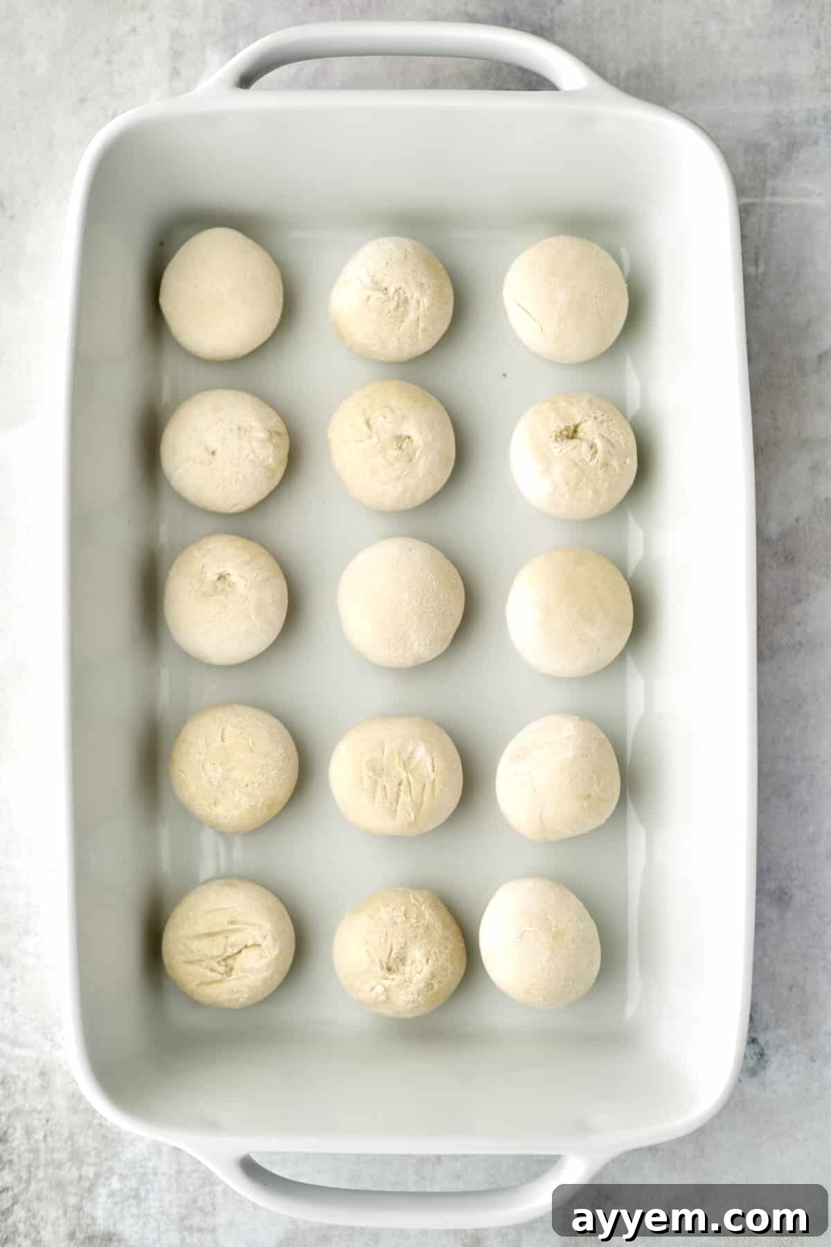 Raw bread rolls arranged in a baking dish, ready for rising.