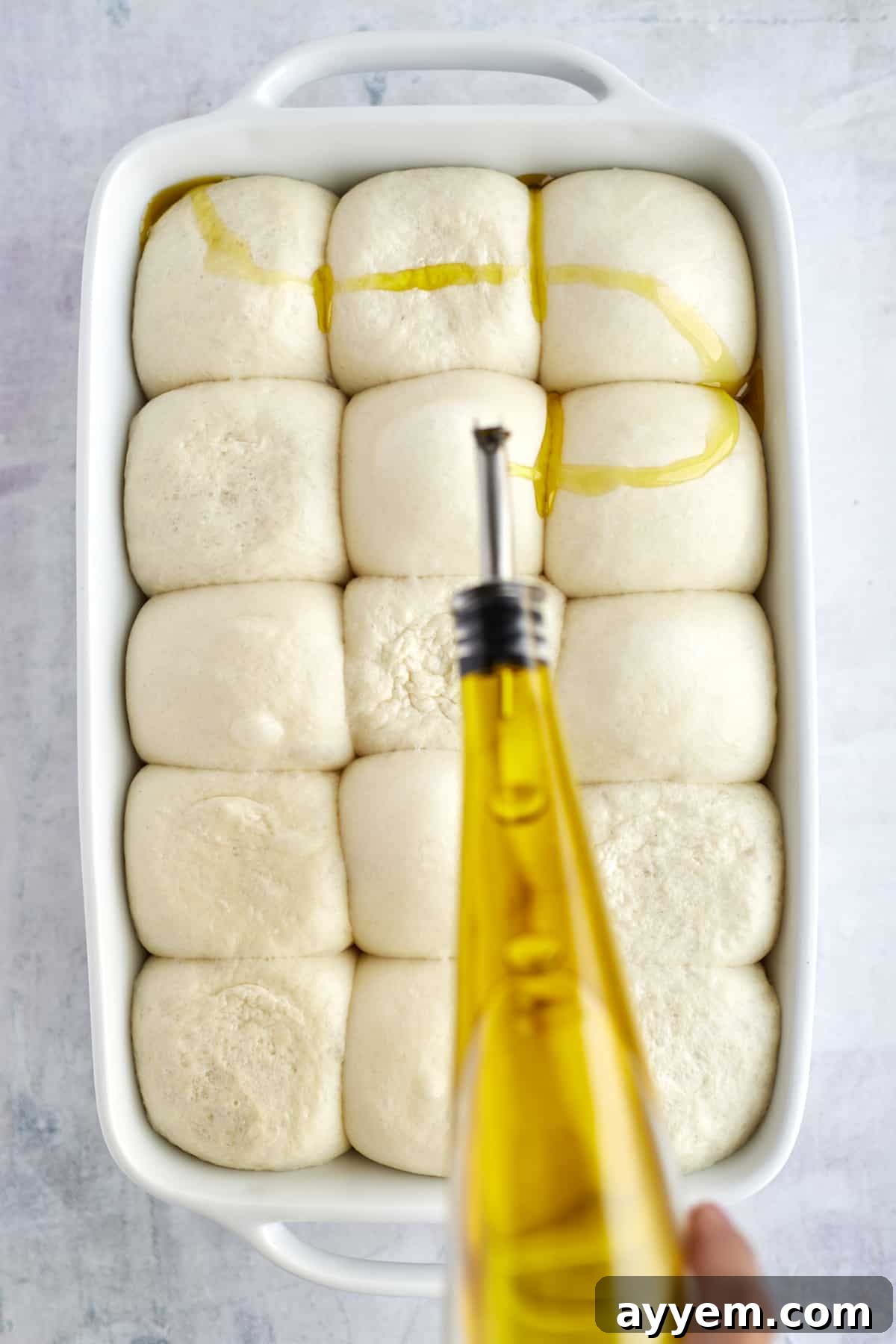 Olive oil being drizzled over raw focaccia dough in a baking dish.