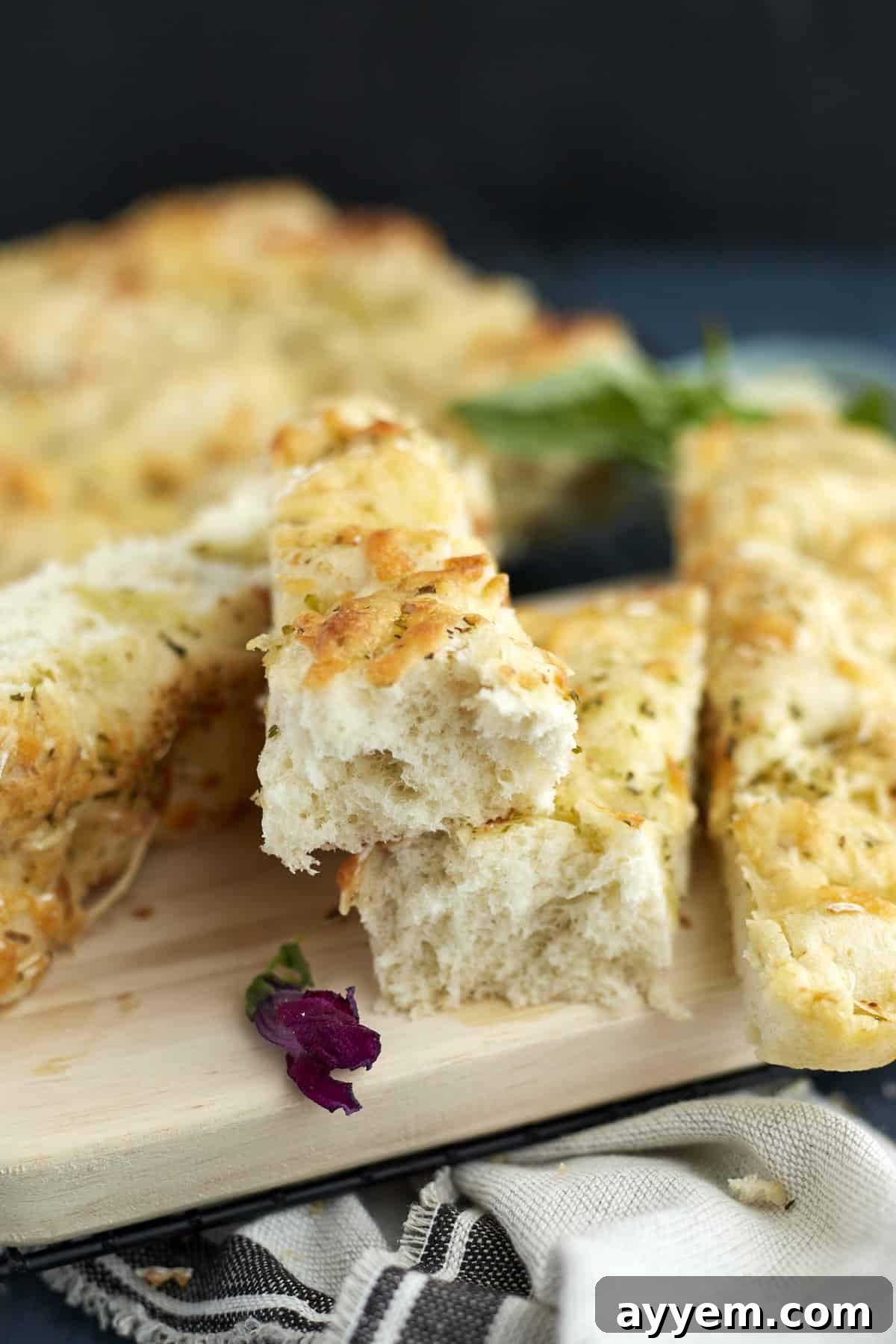 Pieces of no-knead cheesy focaccia bread on a cutting board, garnished with fresh basil.