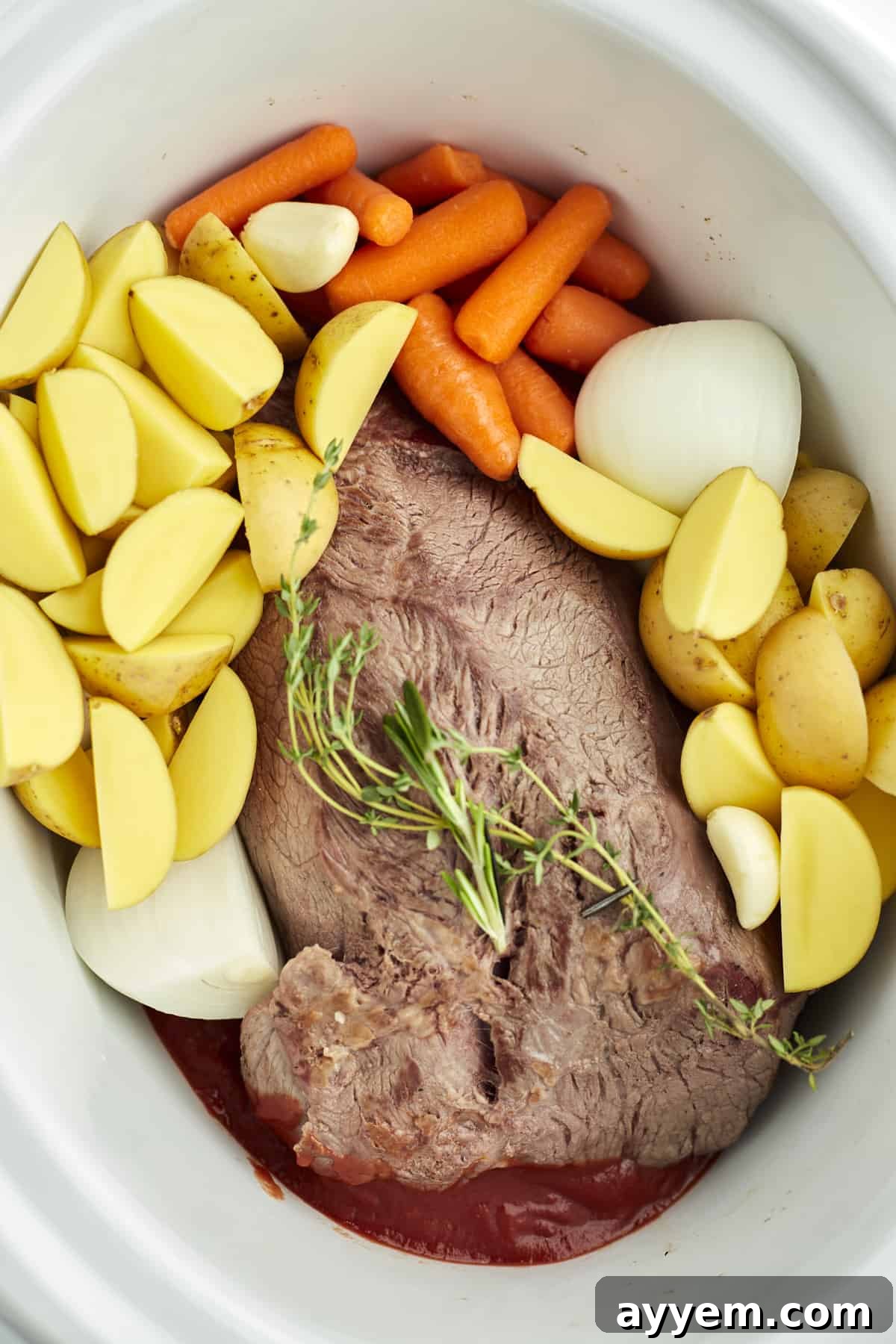 A slow cooker filled with beef pot roast, golden potatoes, carrots, onions, and fresh herbs, simmering gently.