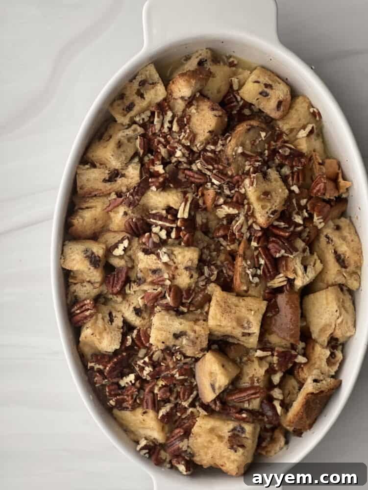 overhead image of unbaked panettone bread pudding with pecan pie filling in an oval baking dish.