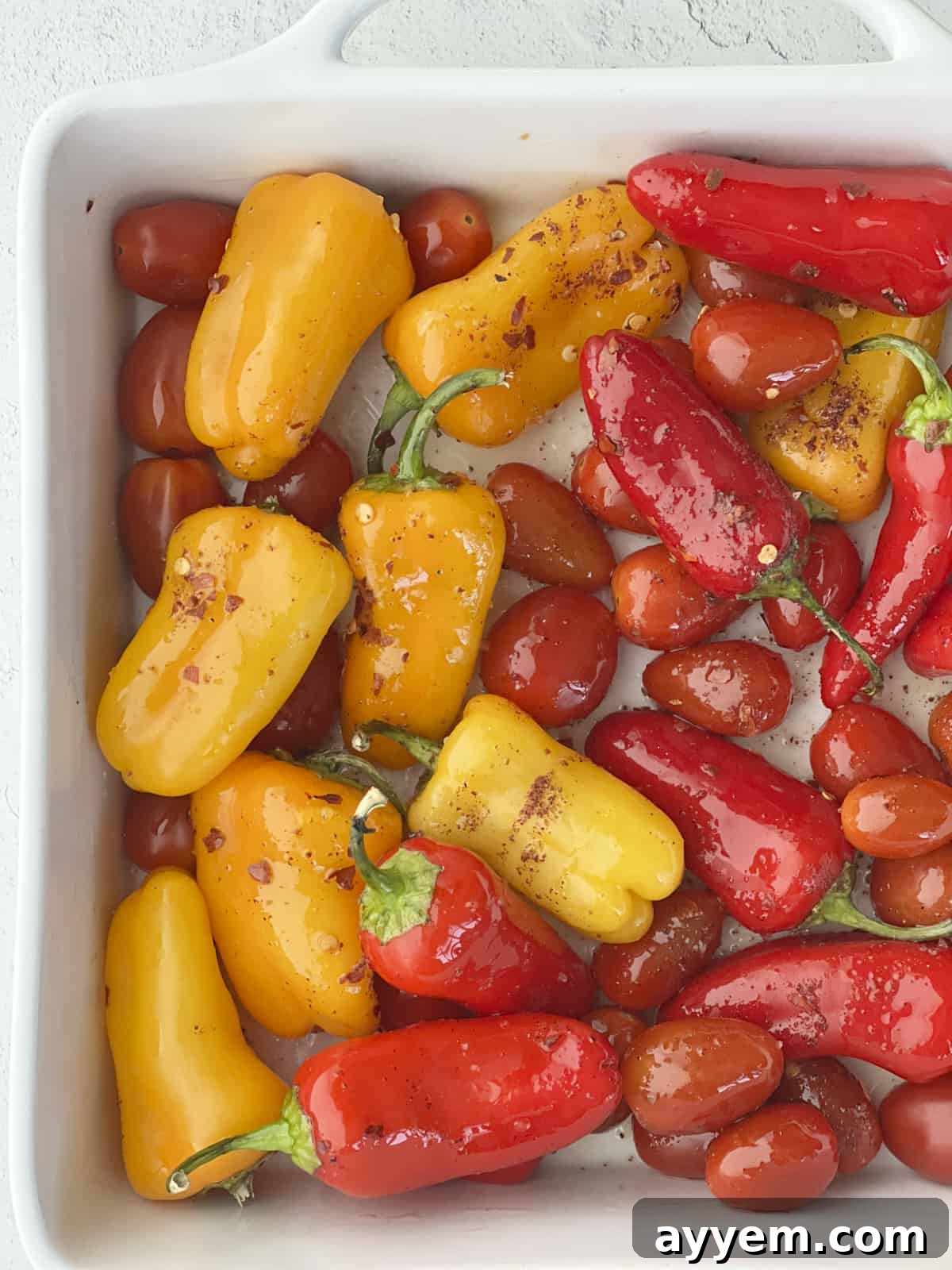 Peppers and tomatoes baking in an oven-safe dish with olive oil and seasonings